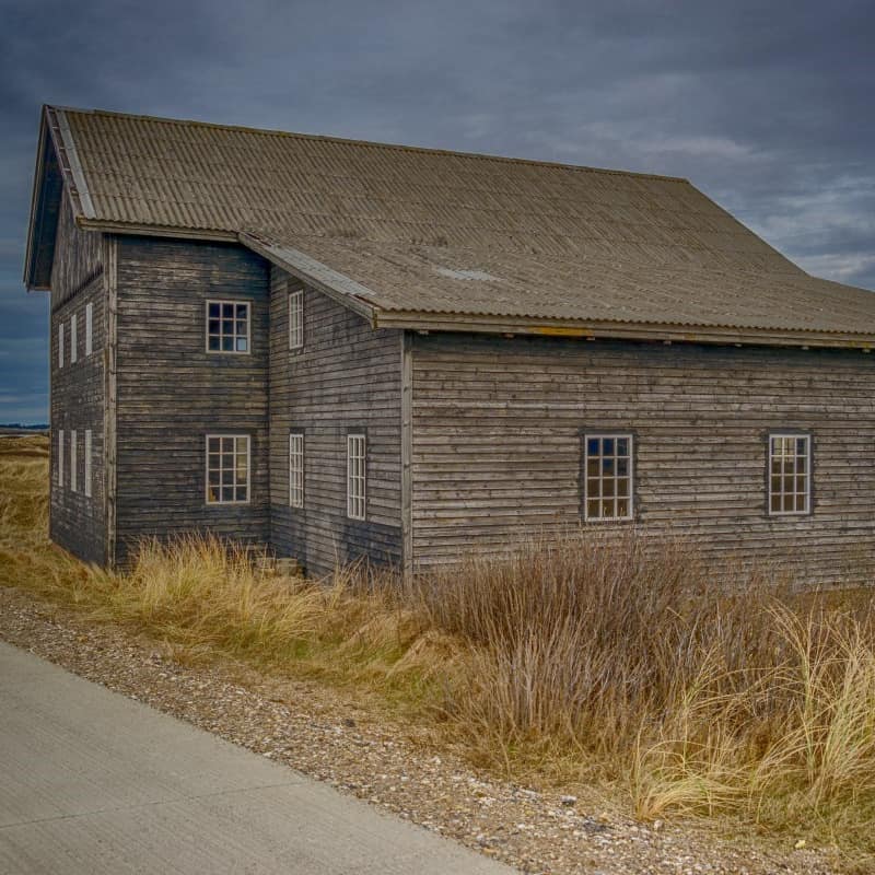 A 2-storey farmhouse with natural wood siding and sloping roof in grassland