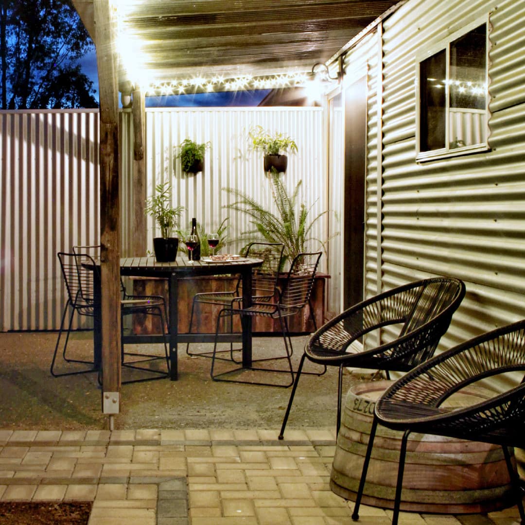 Nighttime view of patio space with brick path, black, round woven chairs, black metal dining set, potted plants.