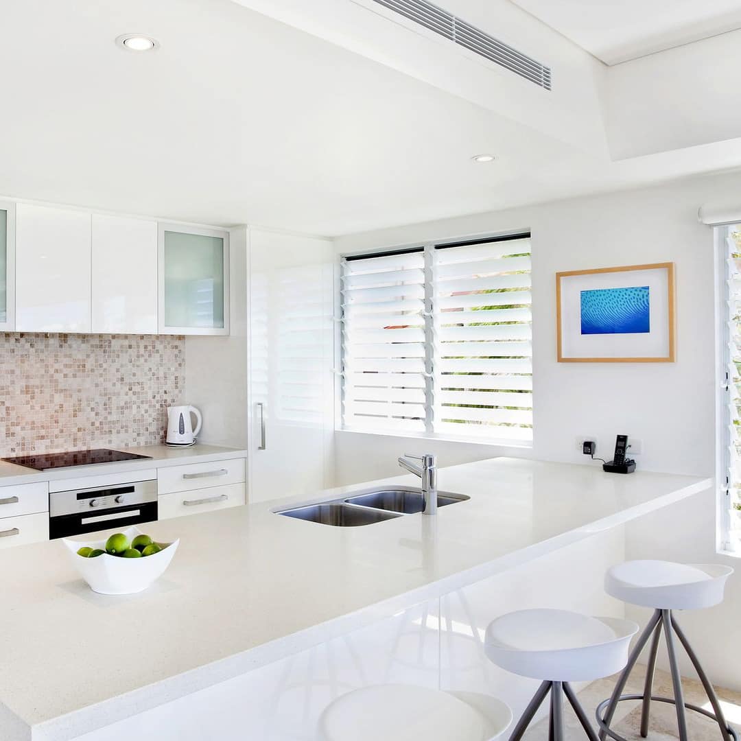 Bright, modern kitchen with hardwood floors, white cabinets and countertops, tan mosaic backsplash.