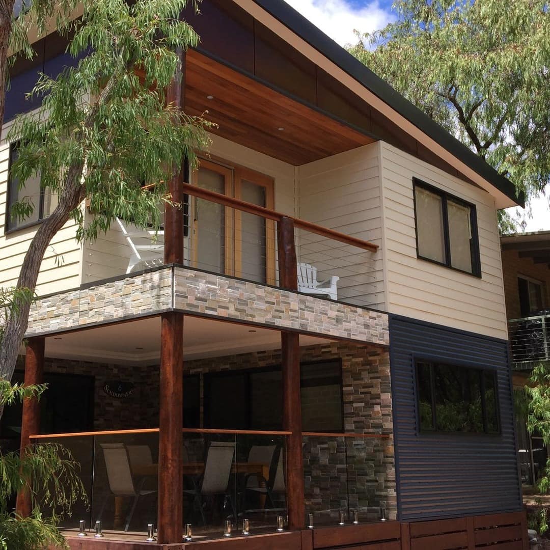 A 2-storey modern wood chalet with a deck on the bottom level and a balcony on the top floor painted in blue and cream.
