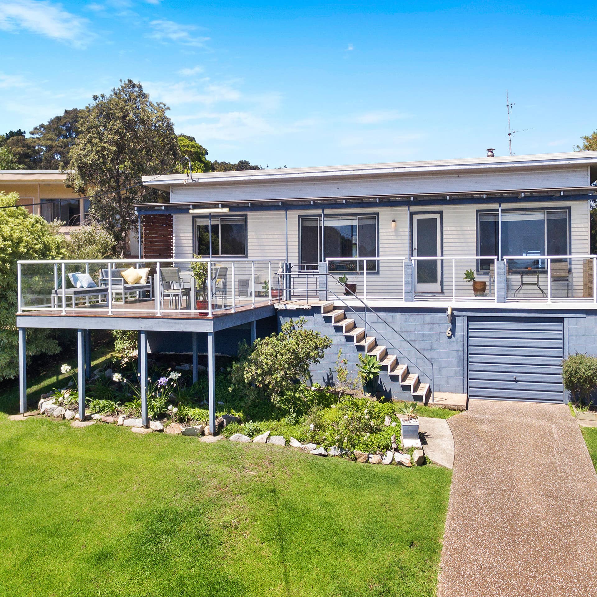 Exterior view of a modern home with a second story deck, glass railing, garage, and a lush lawn and garden.