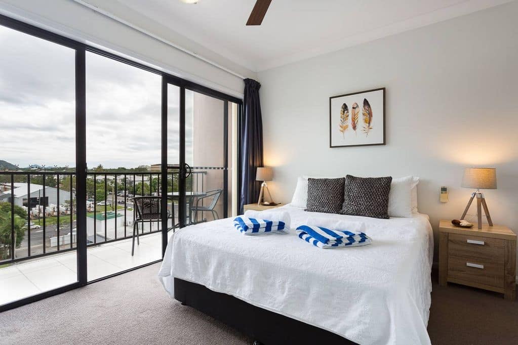 Bedroom with grey carpet, a king size bed, blue quilted bedding, and sliding glass doors to attached balcony.