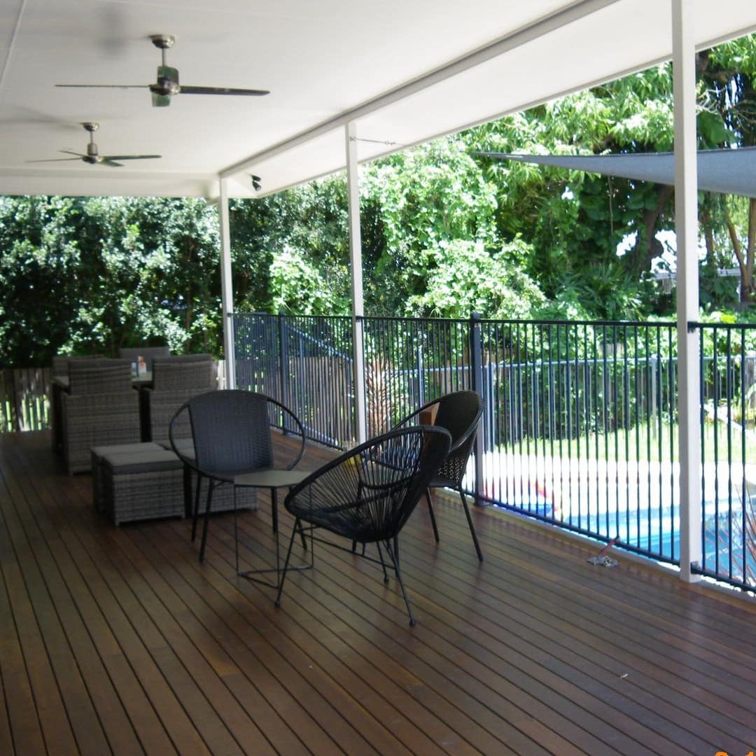 Covered verandah with wood floors and black metal railings, black woven round chairs, overlooking a private pool.