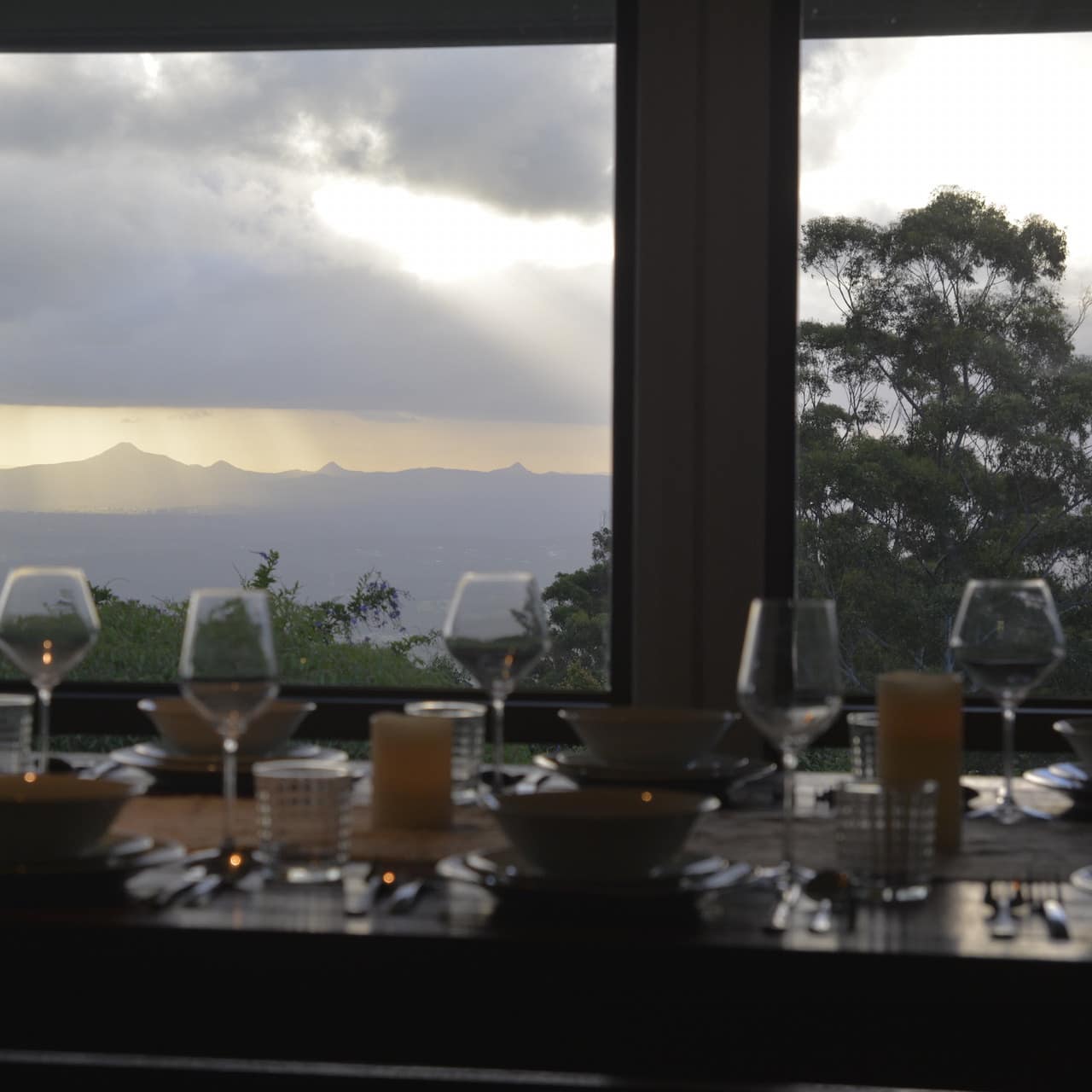 A beautiful mountain scene is visible through the wide windows over a set dining table with wine glasses and bowls.