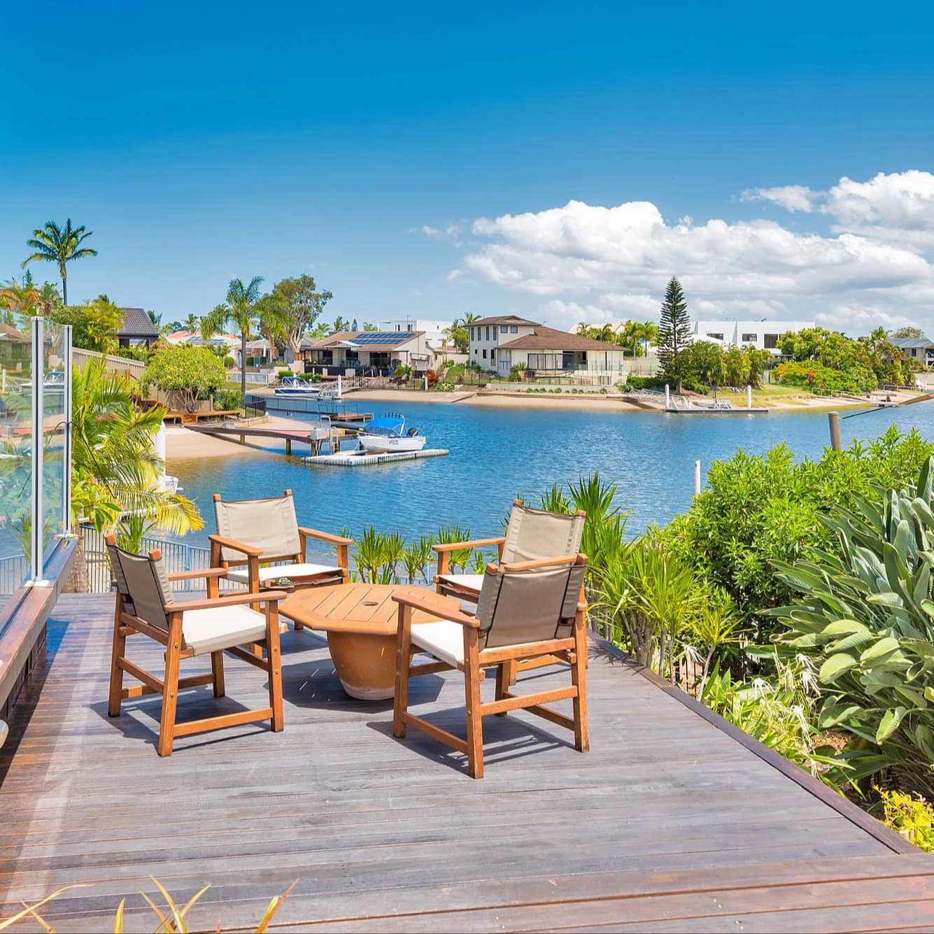 Wooden deck surrounded by tropical plants with a wooden table and chairs overlooking the marina.