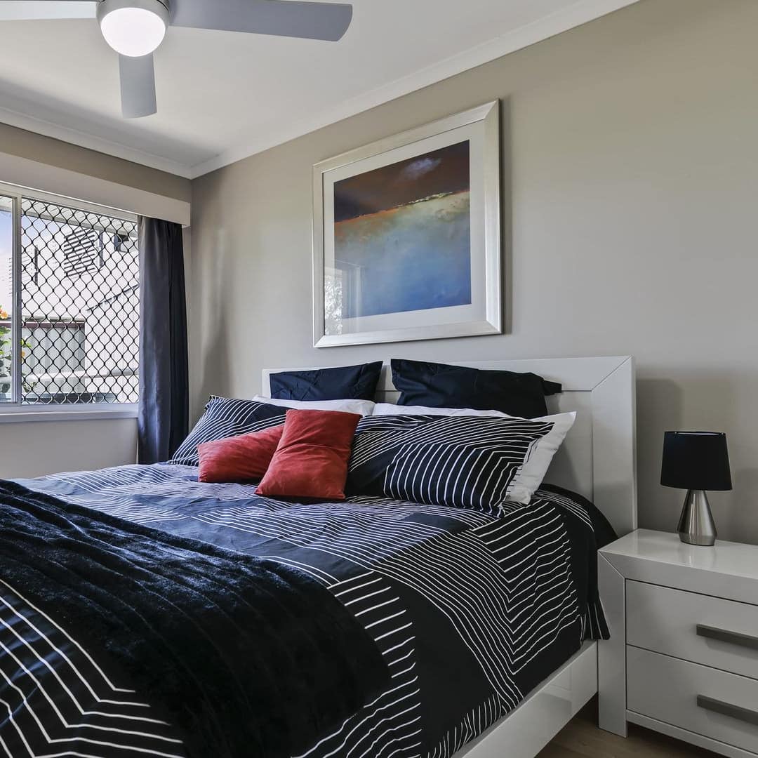 Bedroom with grey walls, hardwood floors, a king size bed, black and white bedding, and a wide window.