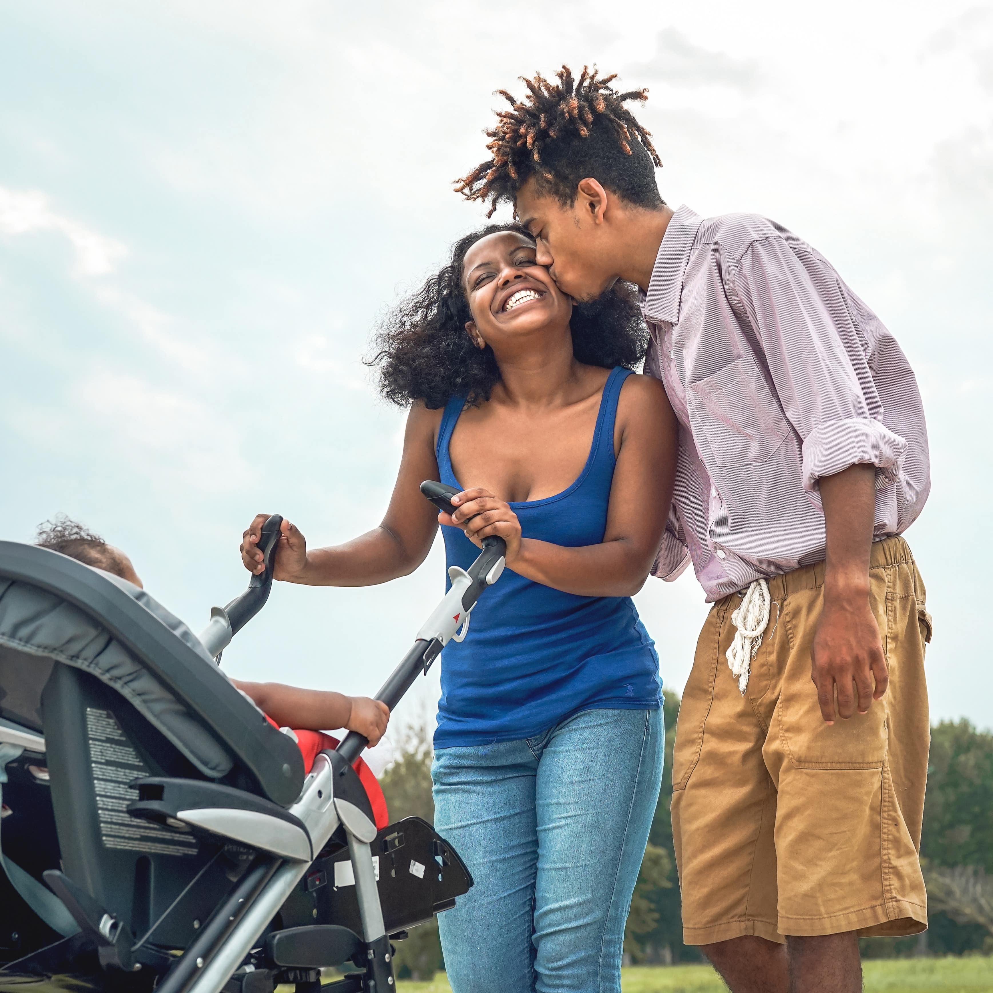 Dad kissing mom on her cheek while she pushes their baby in a pram