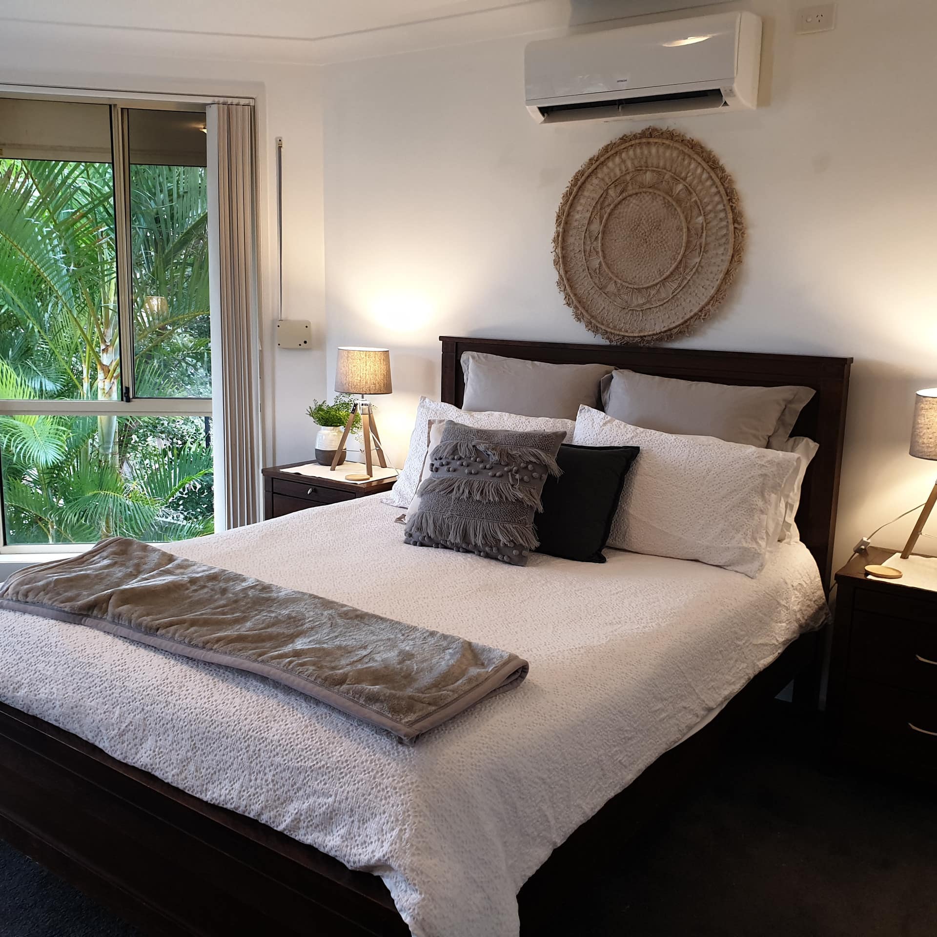 Bedroom with navy blue carpet, king size bed, white and grey bedding, woven wall hanging and tall bay windows.