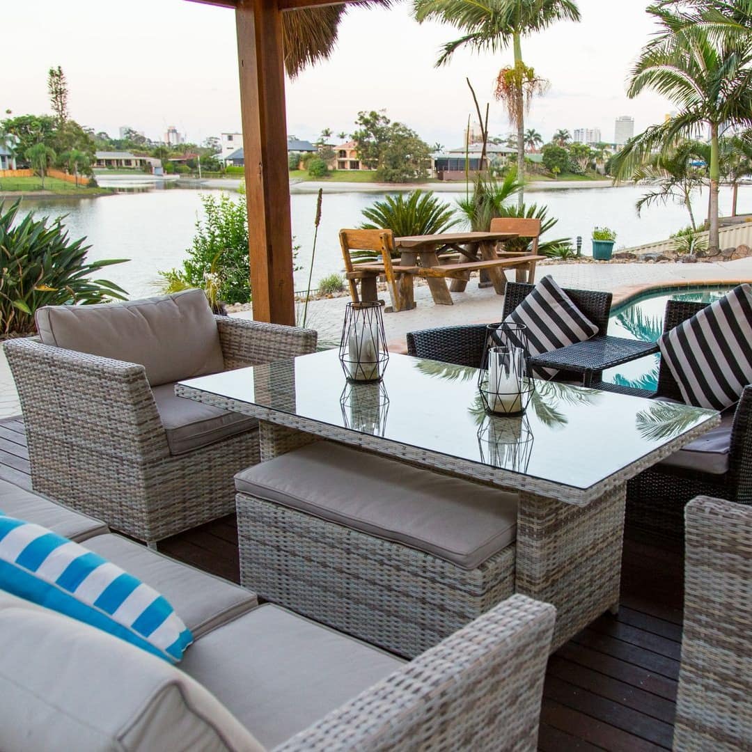 View of a pool and pool deck with wicker furniture, surrounded by palm trees and overlooking the canal.