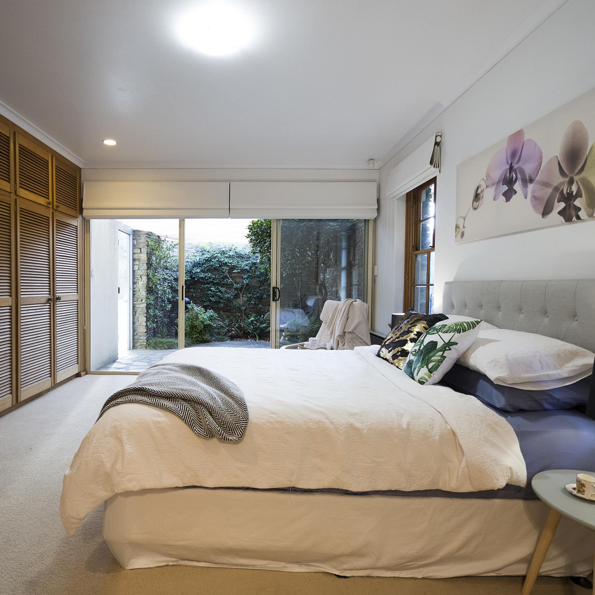Spacious bedroom, beige carpet, wood-panelled closet doors, a king-size bed, white and blue bedding, sliding glass doors.