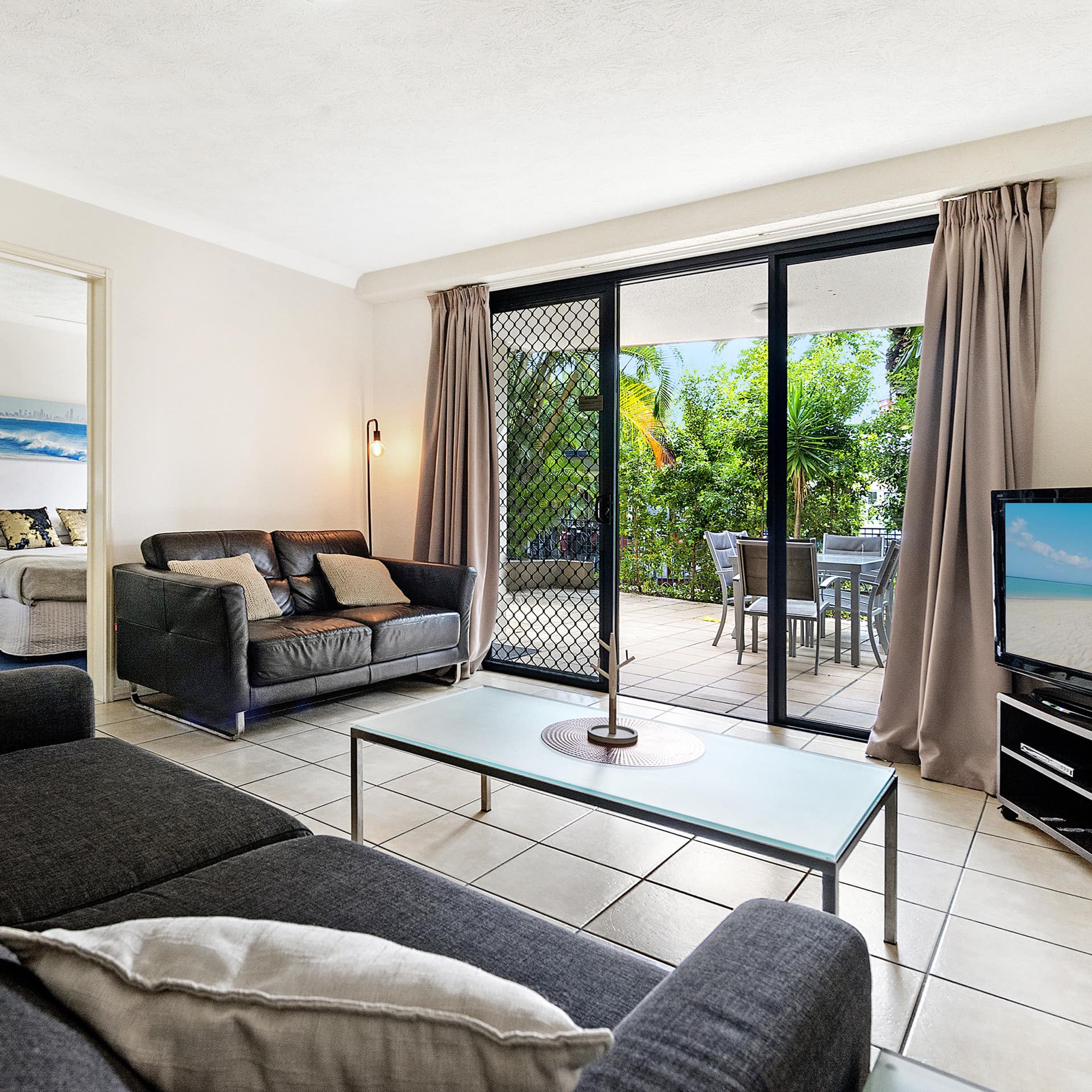 Family-friendly living room of 2-bedroom apartment with tile floor, grey overstuffed sofa, black leather love seat and patio