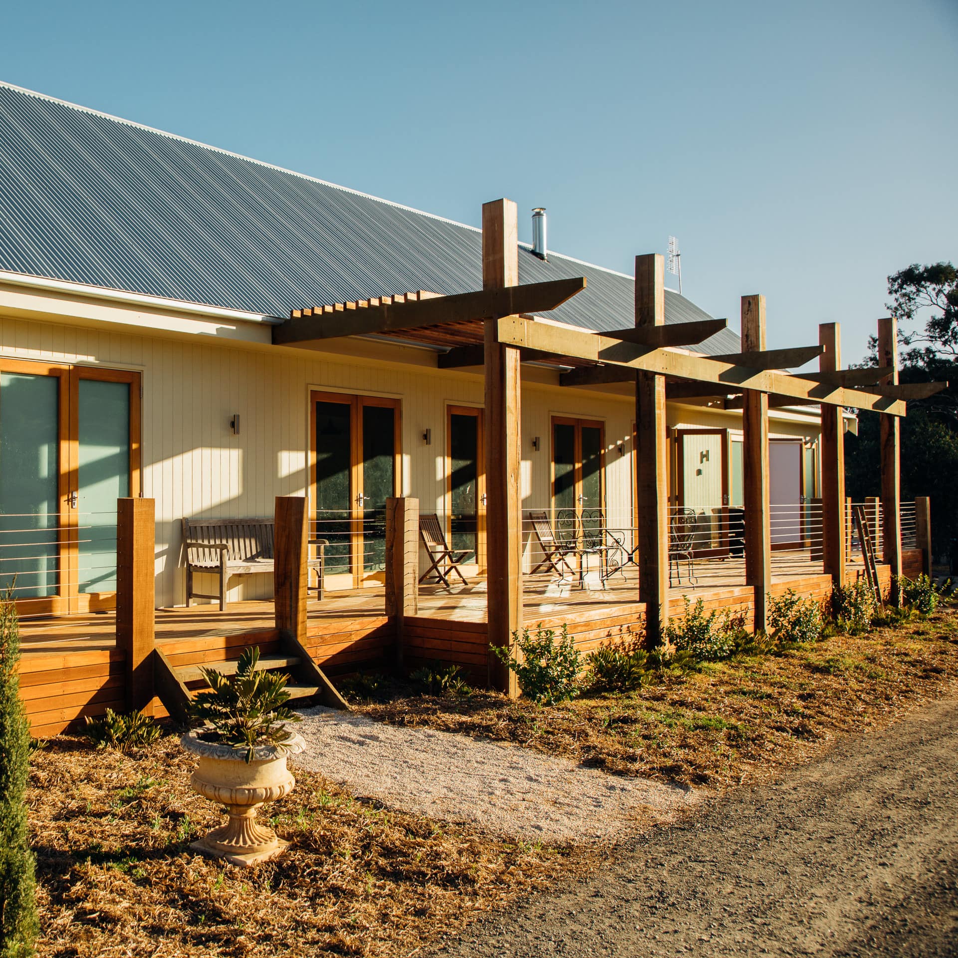 Sunlit white rustic cottage, partially covered wooden deck with wooden seats and benches.