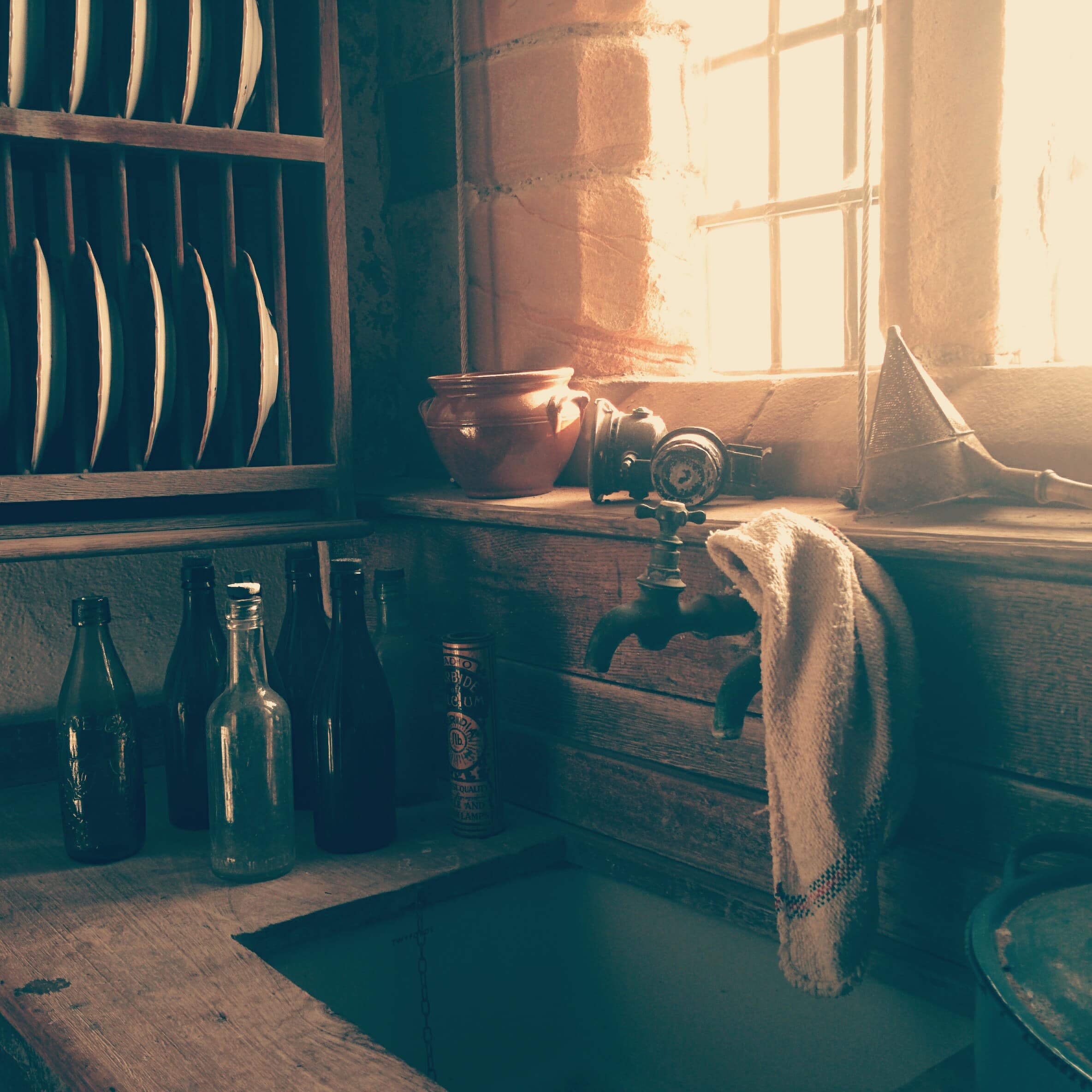 Farmhouse kitchen with an old-fashioned spigot and handle, wood countertop, plate rack and window glowing pink