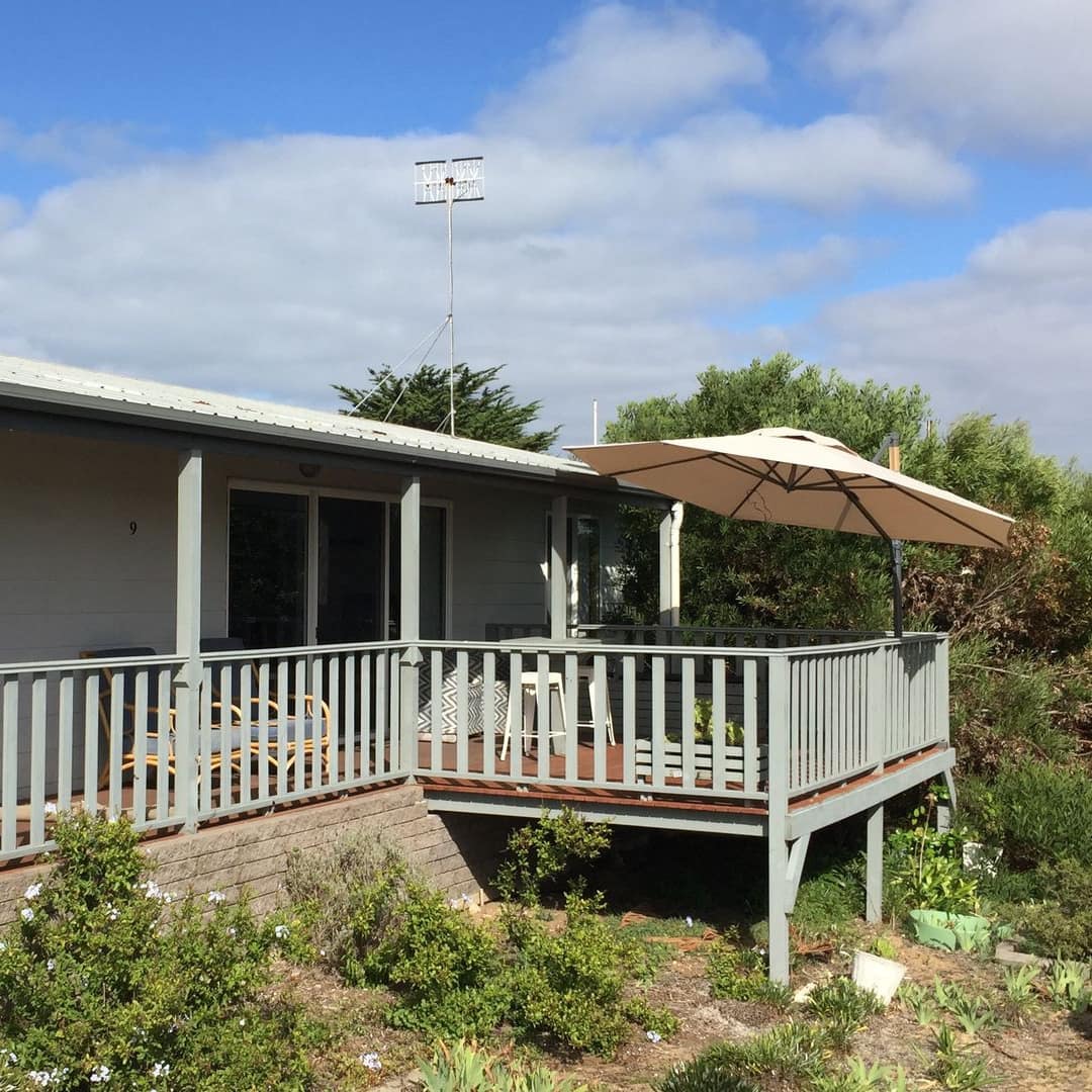 Ranch-style home with white panel siding, grey trim, a partially covered deck, and front lawn.