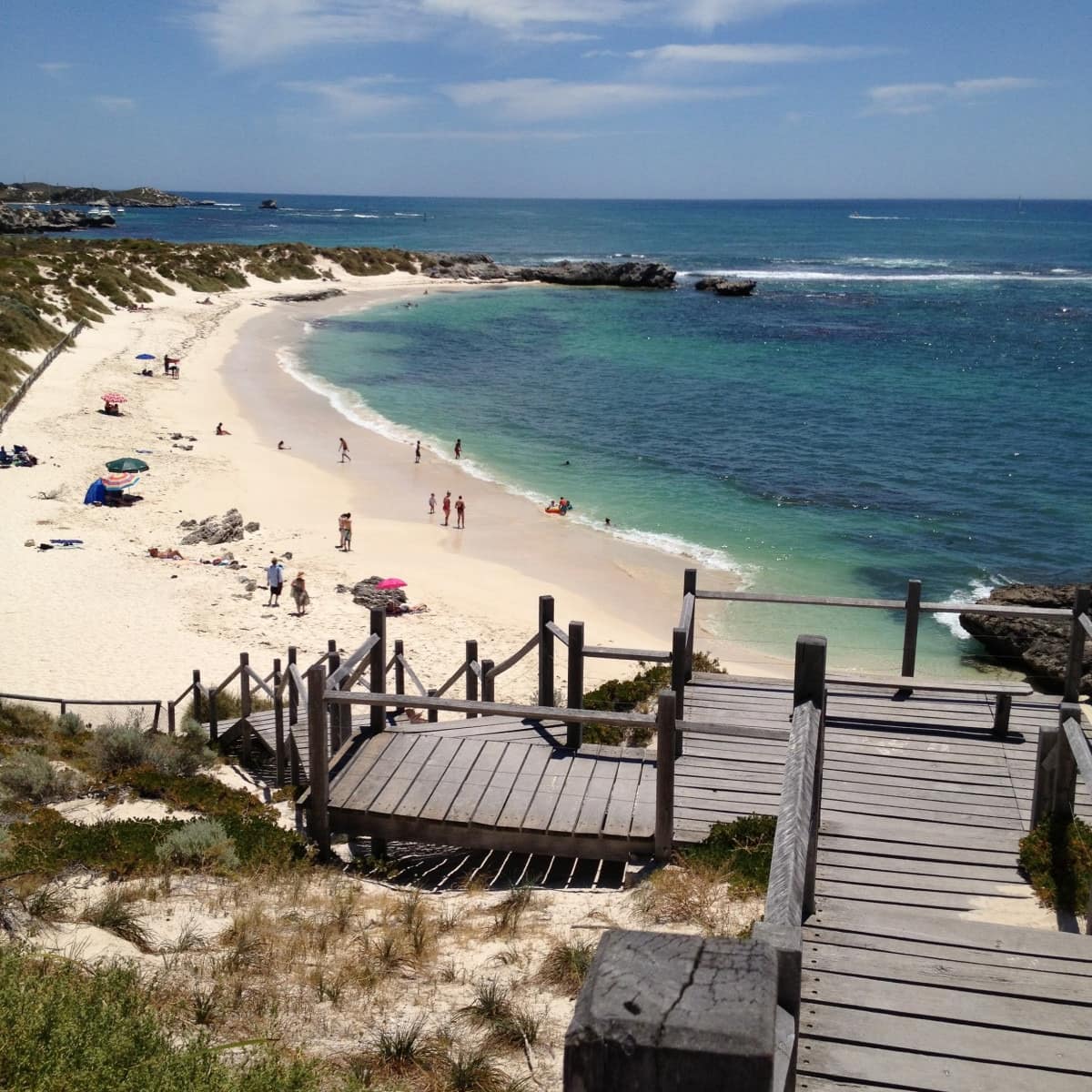 Rottnest Island beach with wooden stairway to beachfront and people enjoying relaxing on the sand and playing in the water