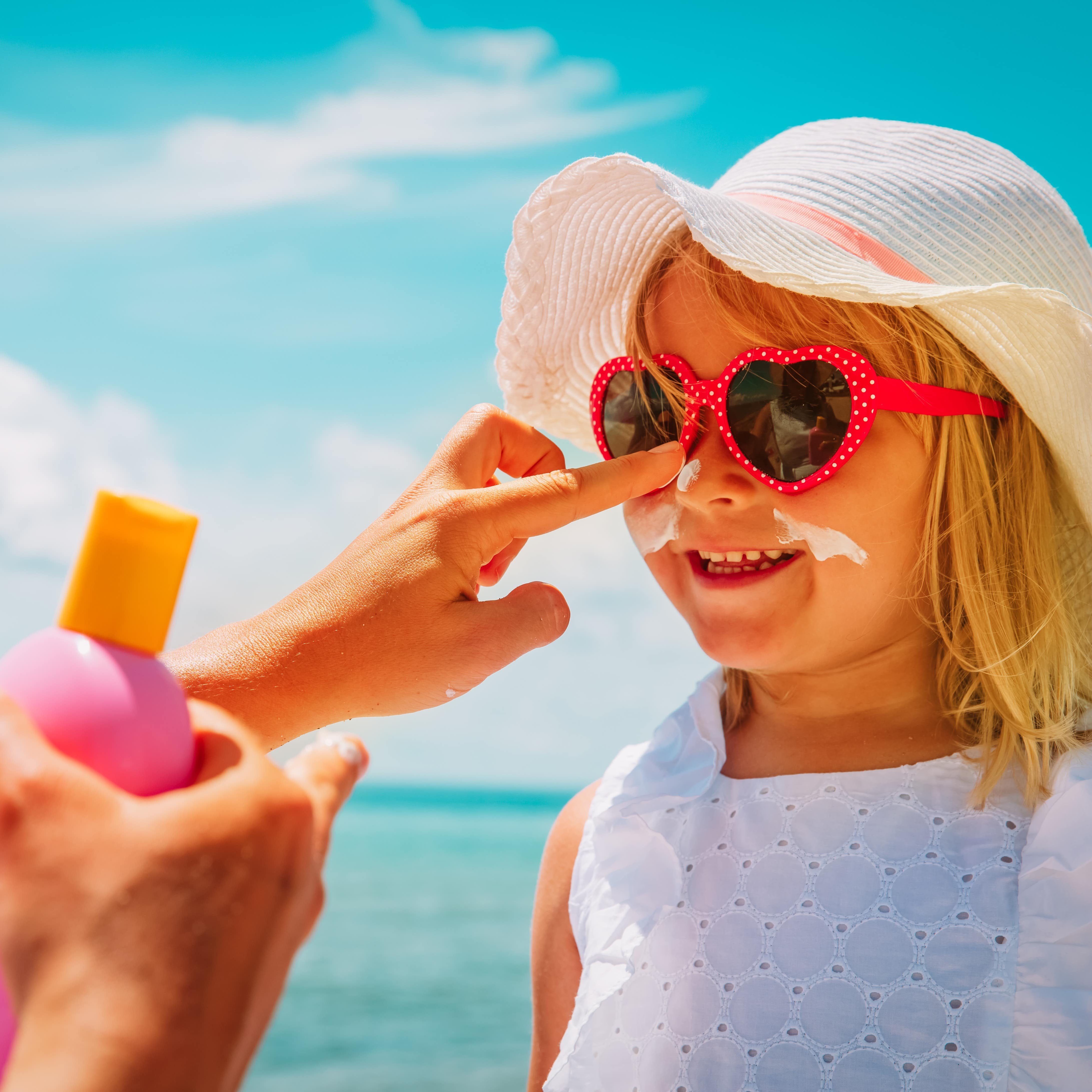 Little girl getting sunscreen and hat for protection from the sun