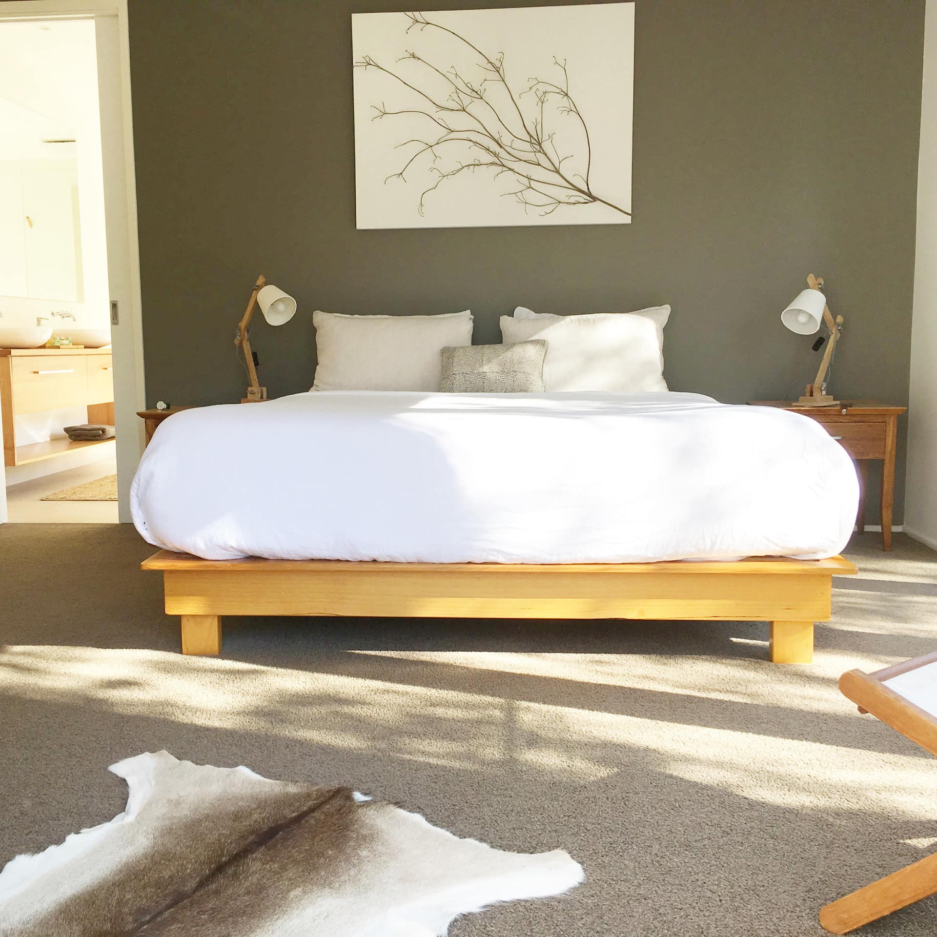 Sunny bedroom with grey carpet, dark green walls, a king-size bed and fur rug.