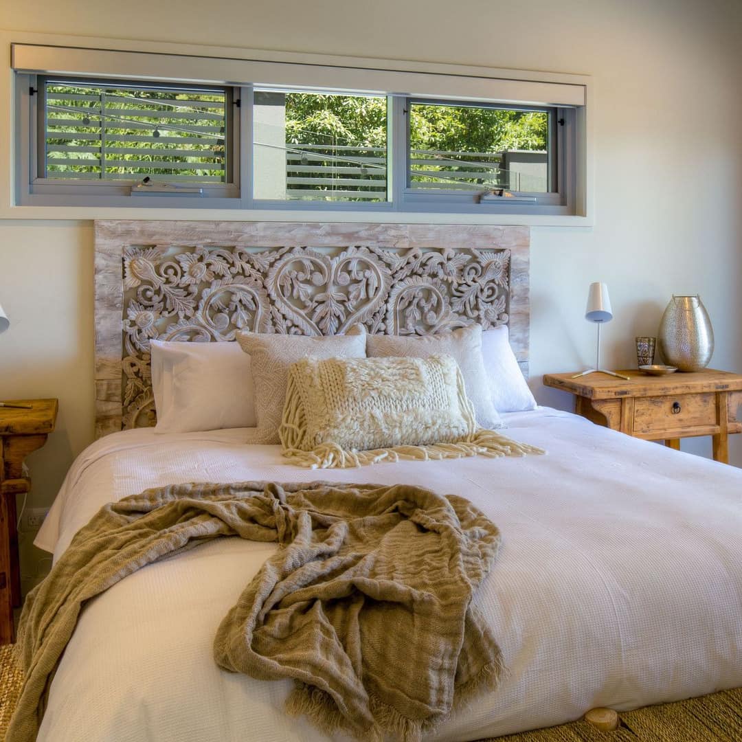 Rustic bedroom with a king size bed with white and tan bedding and carved wood headboard, and wooden bedside tables.