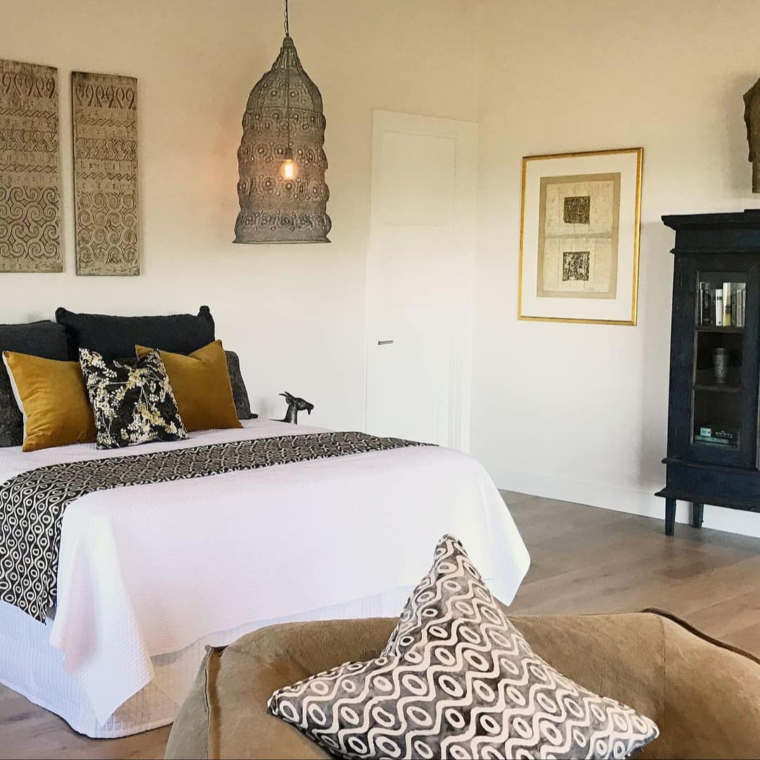 Queen bed with white linens and black and gold throw pillows, Southeast Asian decor, and a black curio cabinet.
