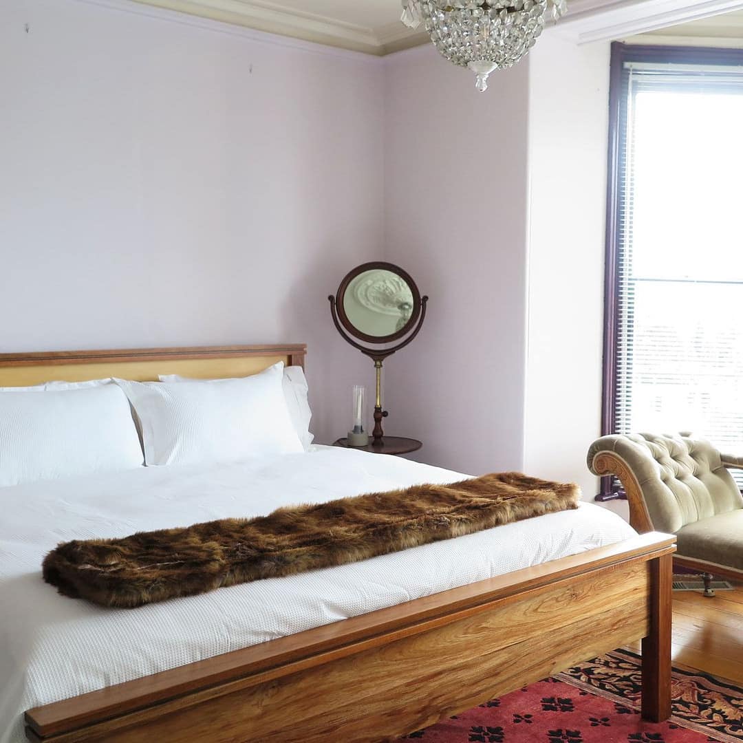 Charming bedroom with lavender walls, hardwood floors, a wood-framed king size bed, and an antique chaise lounge.