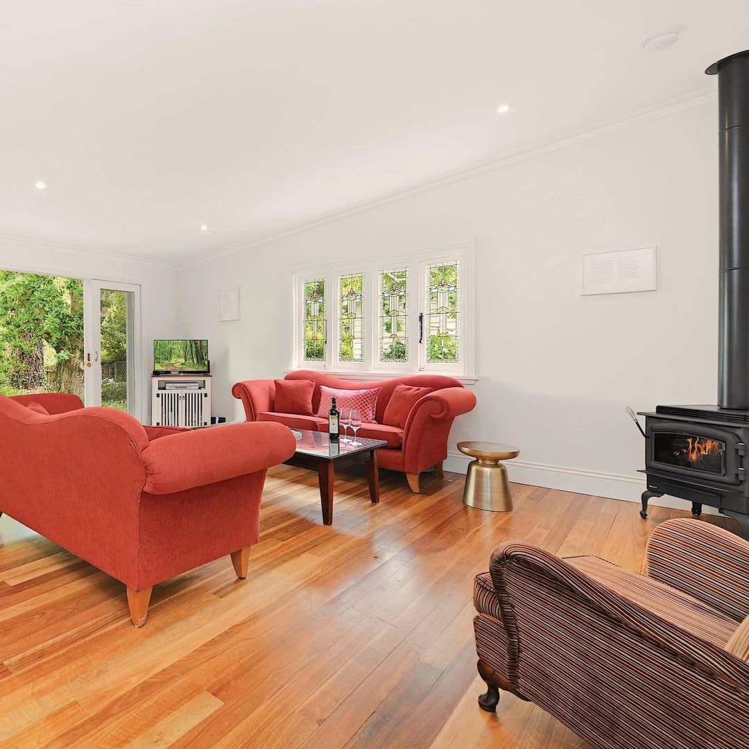 Living area of 3-bedroom cottage with red overstuffed sofas, a chaise lounge and stove fireplace