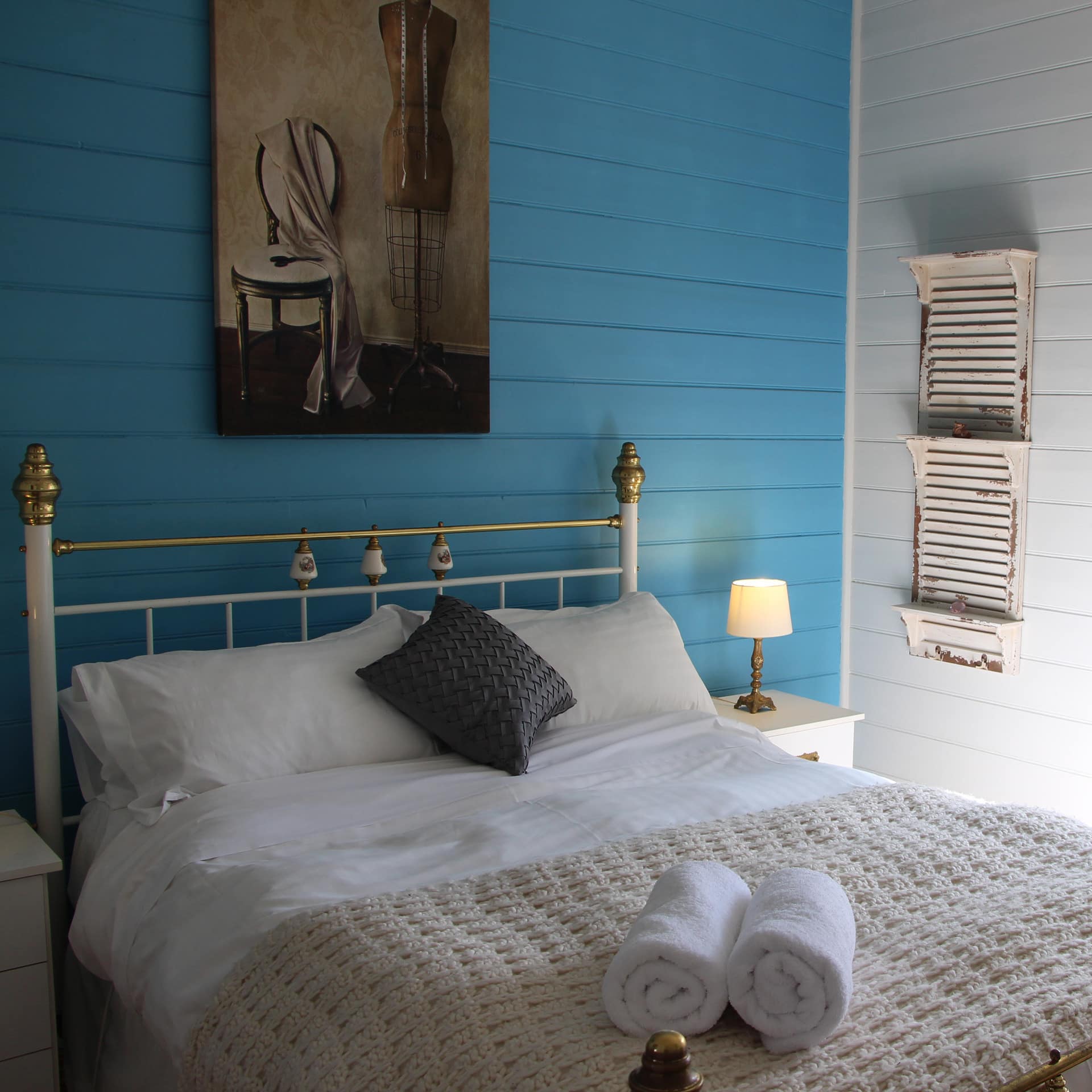 Master bedroom of a 1900s cottage with bright blue wood walls, original wood floors, and a brass bed with white bedding.