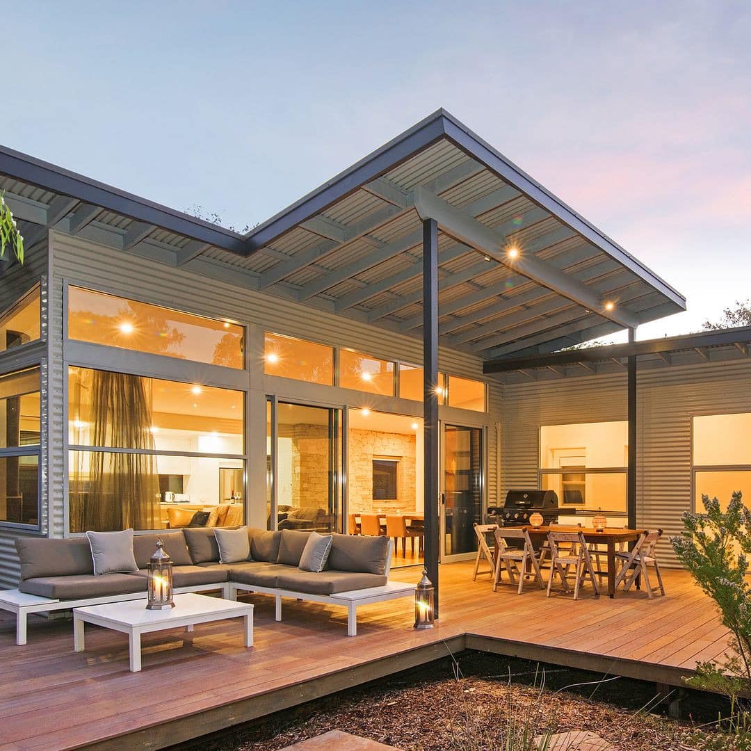 View of a modern home with a wooden deck, tan sectional and wooden dining set.