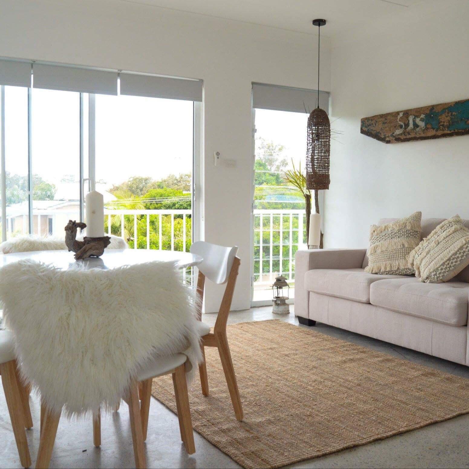 Living room with grey stone floors, beige sofa, white dining set, woven tan rug, and sliding glass doors to balcony.