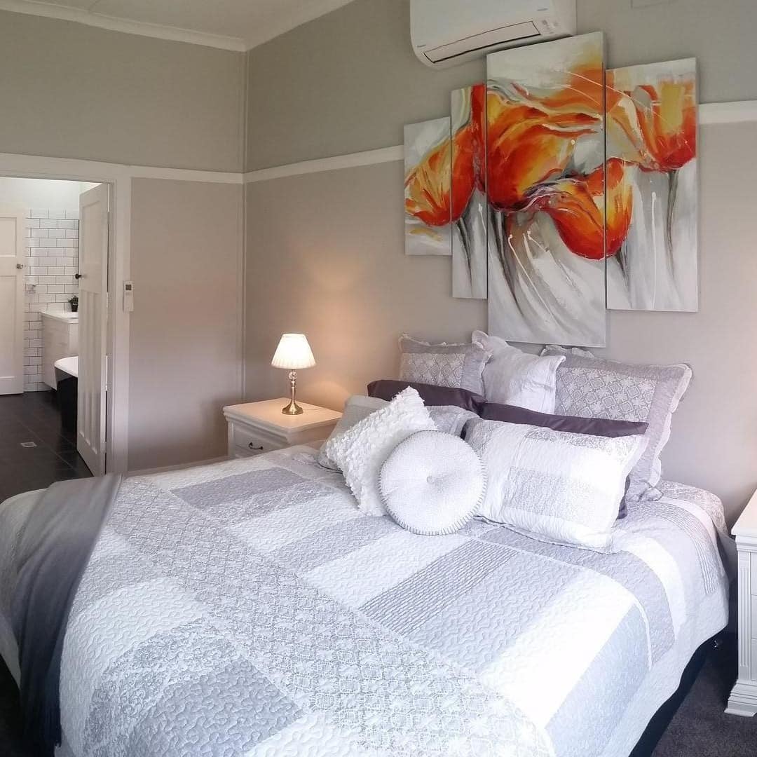 Bedroom with a king size bed, dark hardwood floors, light grey walls, grey and white bedding, and a floral painting.