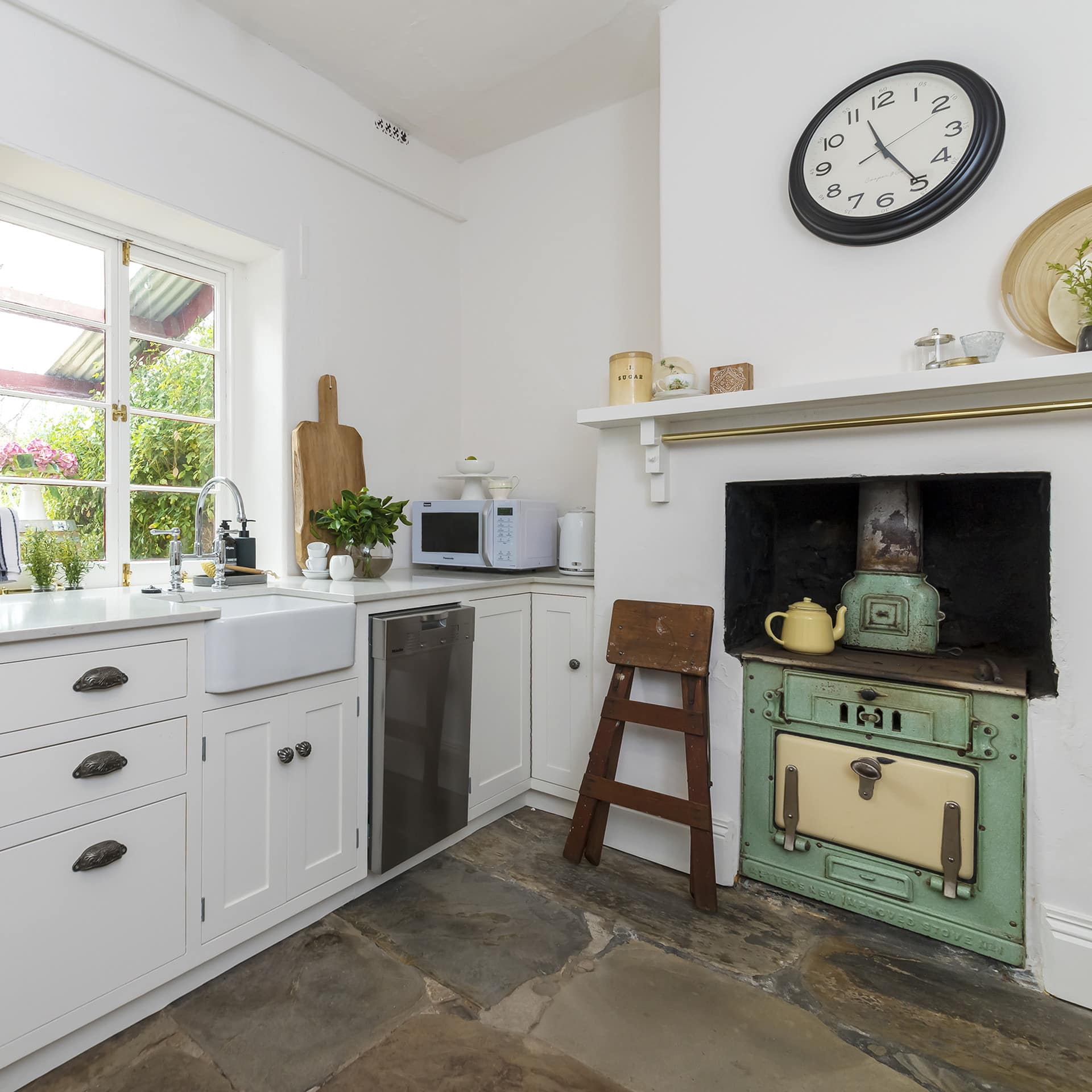 Rustic kitchen with natural stone floors, white walls, white cabinets and countertops, and a green vintage stove.