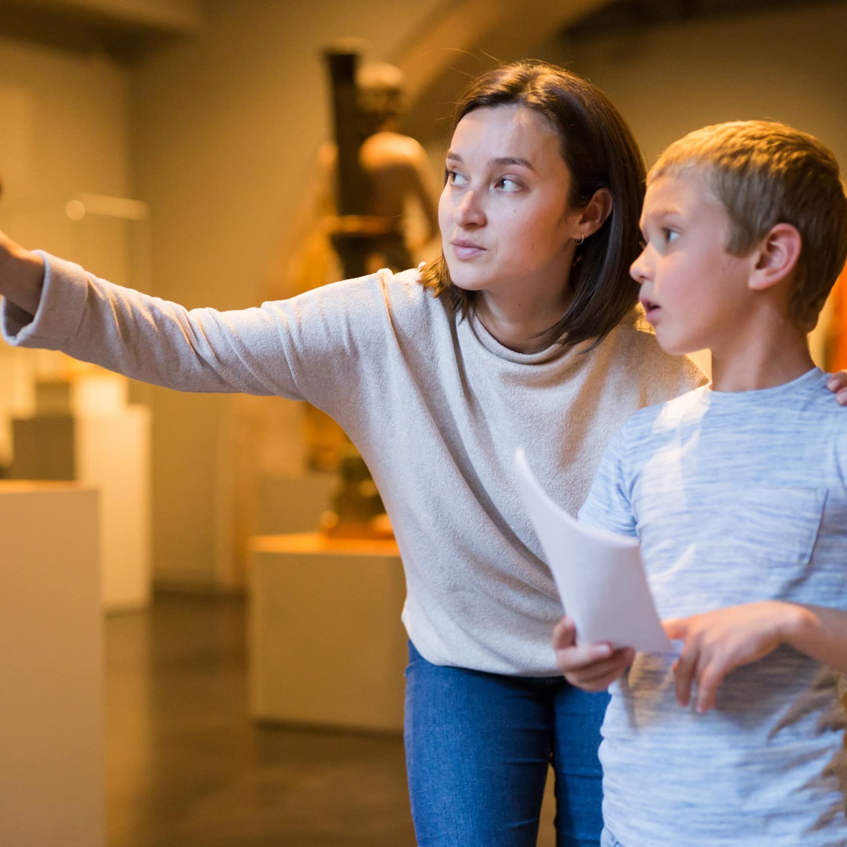Woman with son observing with interest sculptures exhibition in art museum, pointing to something interesting
