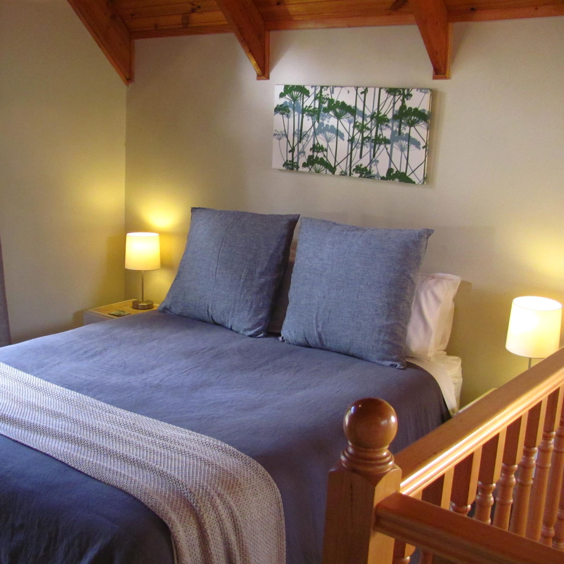 Bedroom with light green walls, vaulted ceiling with exposed beams, queen size bed, blue and white bedding.