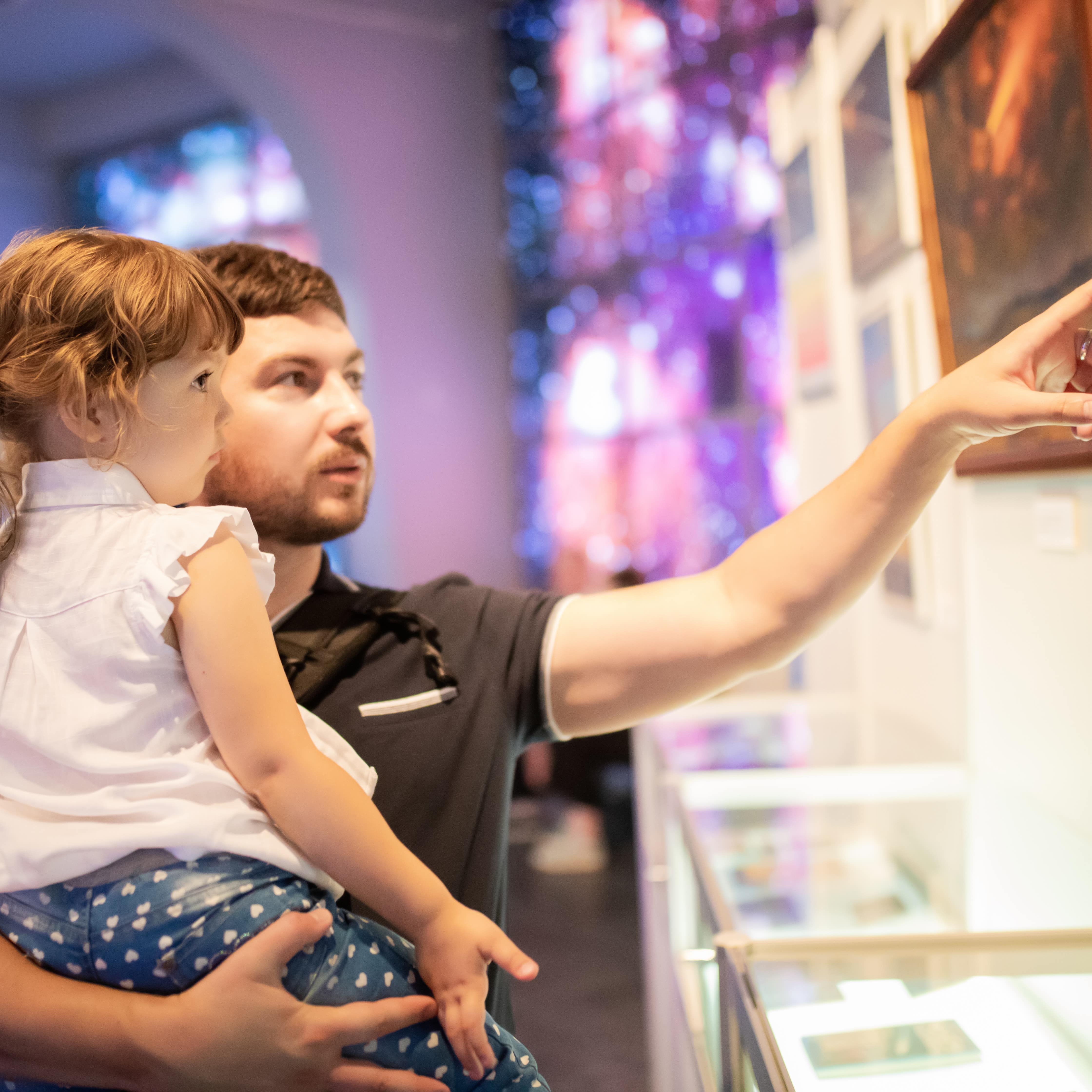 Father holding young daughter in arms and pointing to an exhibit in a museum