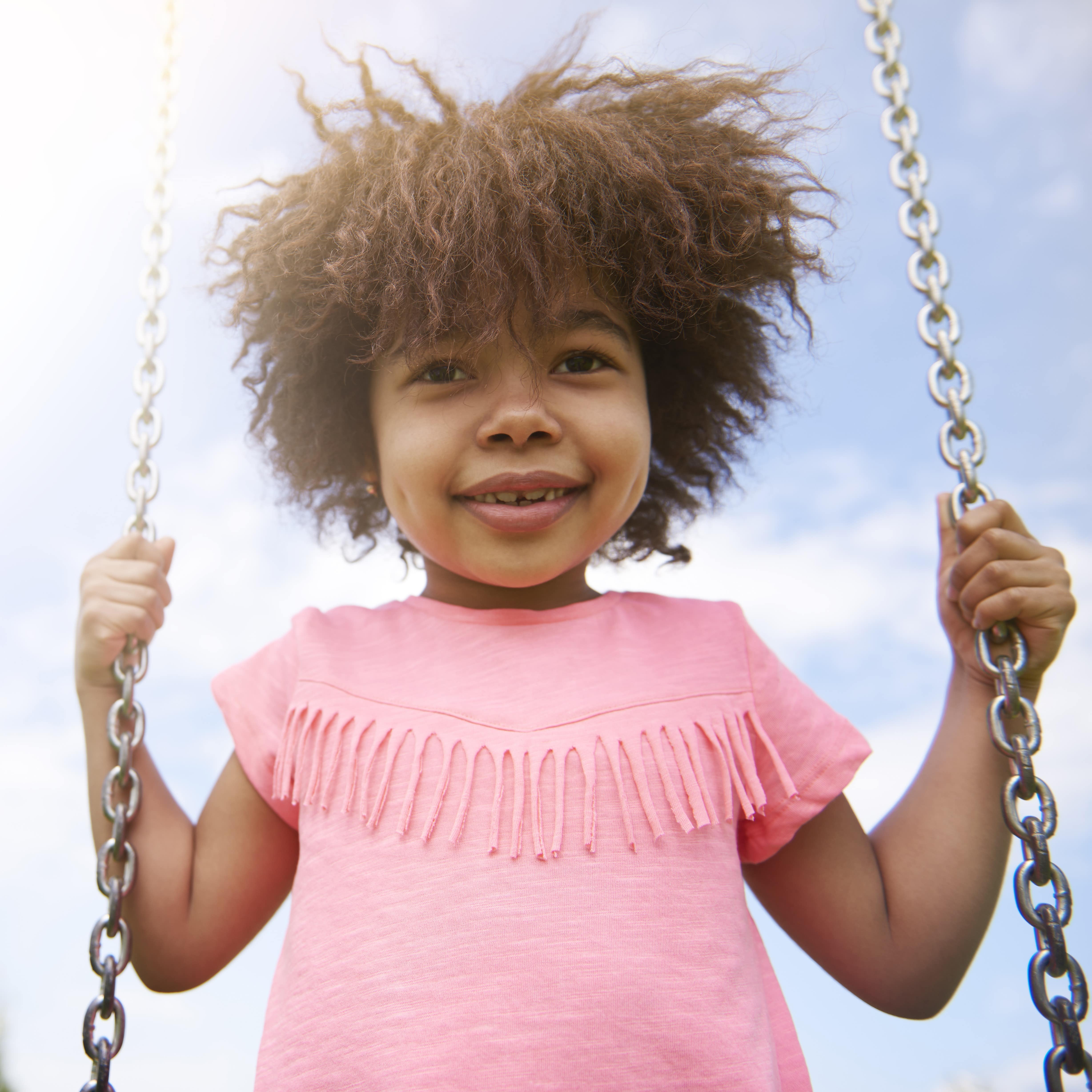 Smiling little girl with pink dress on swing at park