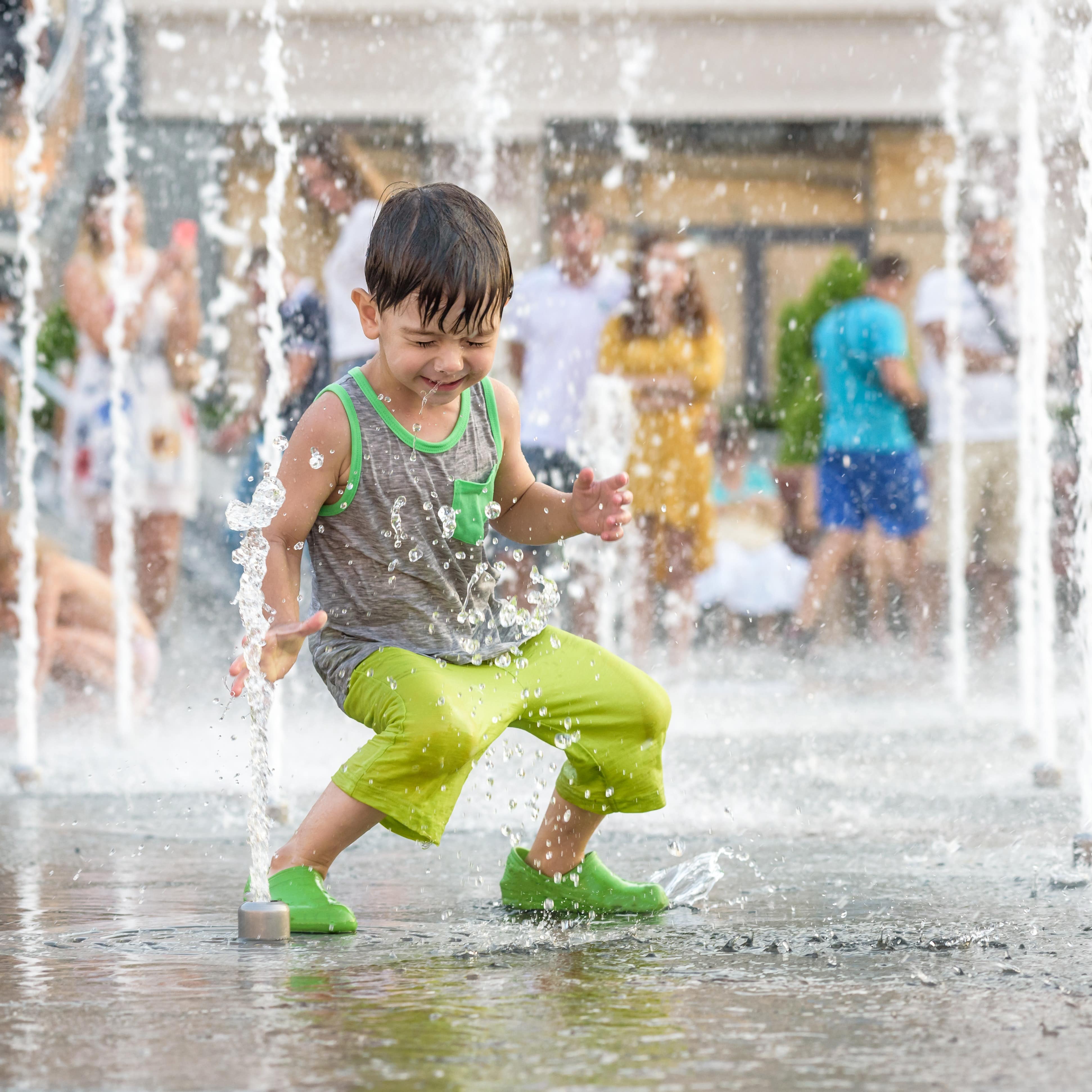 Young boy with eyes closed squatting between water jets in spray fountain