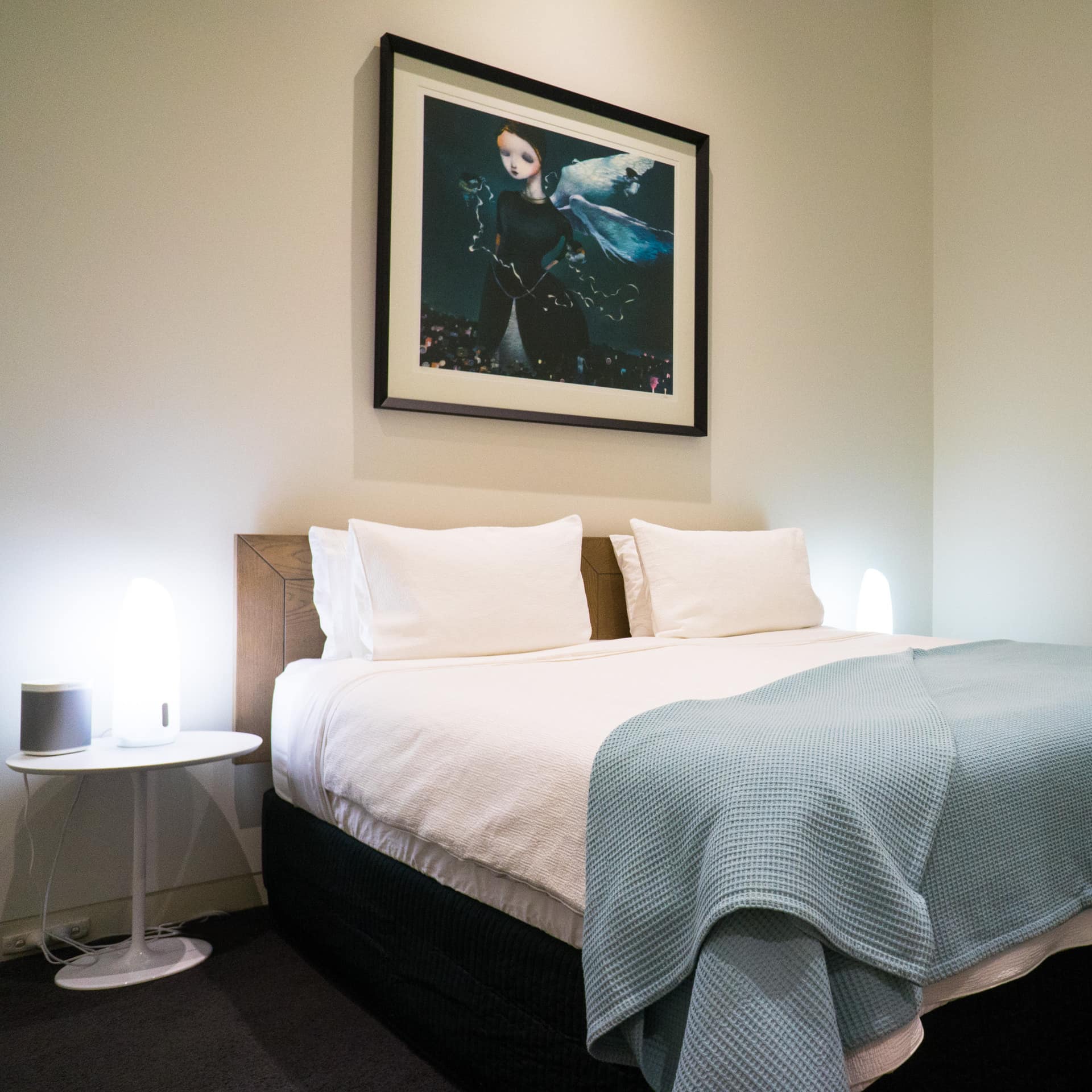 Bedroom with black carpet, white walls, a king size bed, white and blue bedding, and round bedside tables.