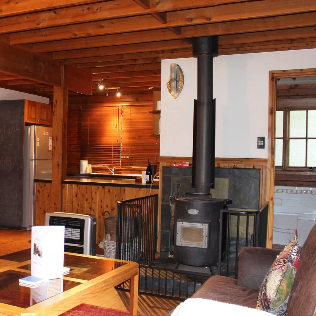 Living room of rustic cabin with hardwoods throughout, fireplace, soft leather sofa and a view of kitchen and dining areas