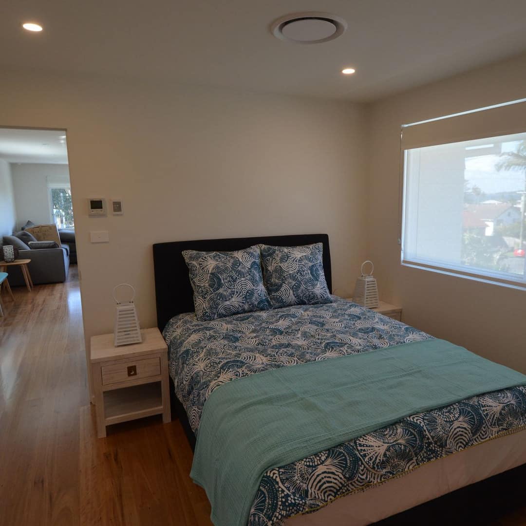 Neatly made bed with blue and aqua comforter in bright, white room with long, rectangular sliding window