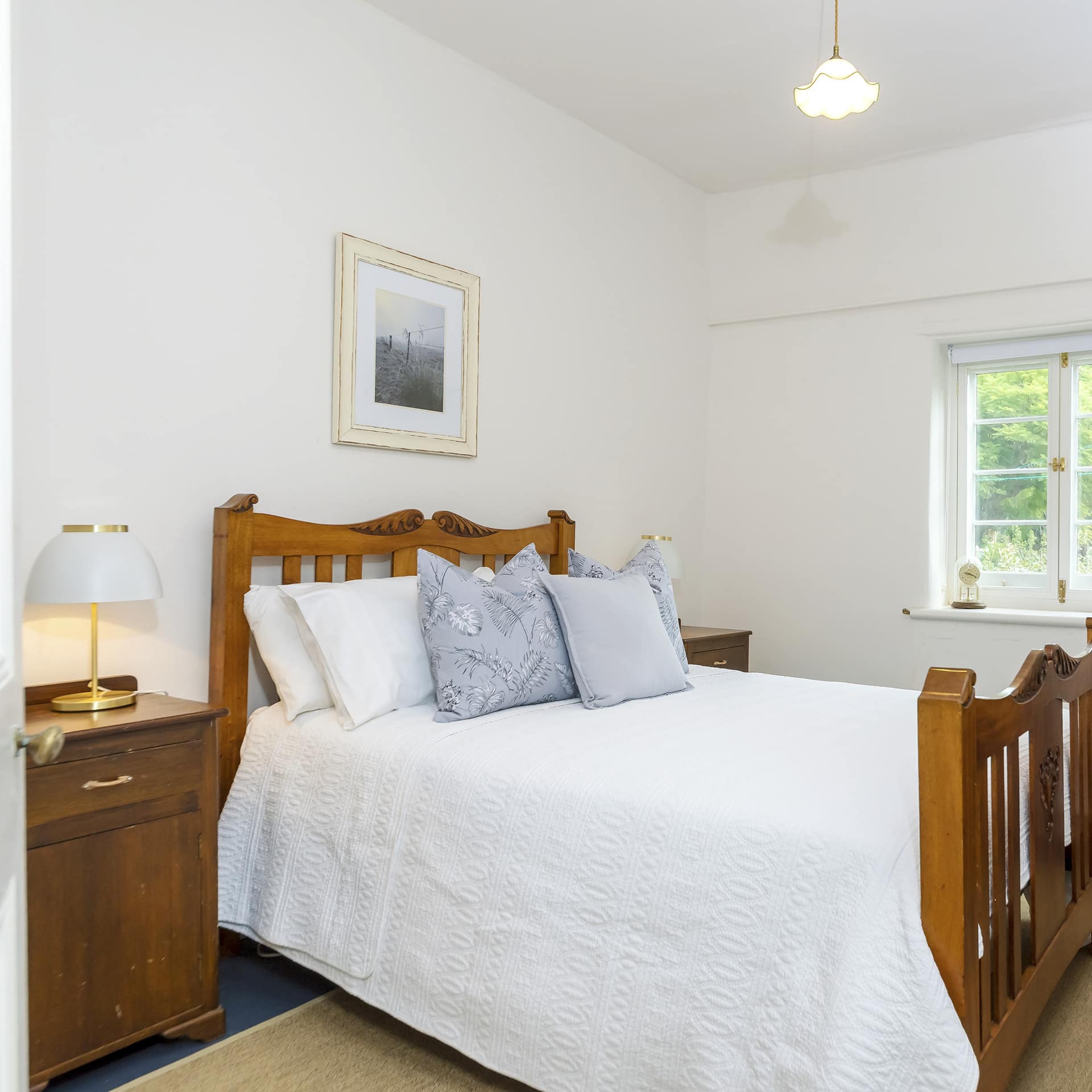 Bedroom with wood-framed king size bed, white bedding, and vintage wooden furniture.