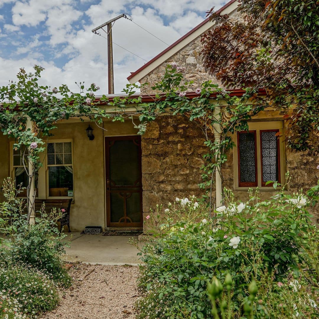 Charming cottage with natural stone siding, gravel path to covered front porch with ivy growing over the porch beams.