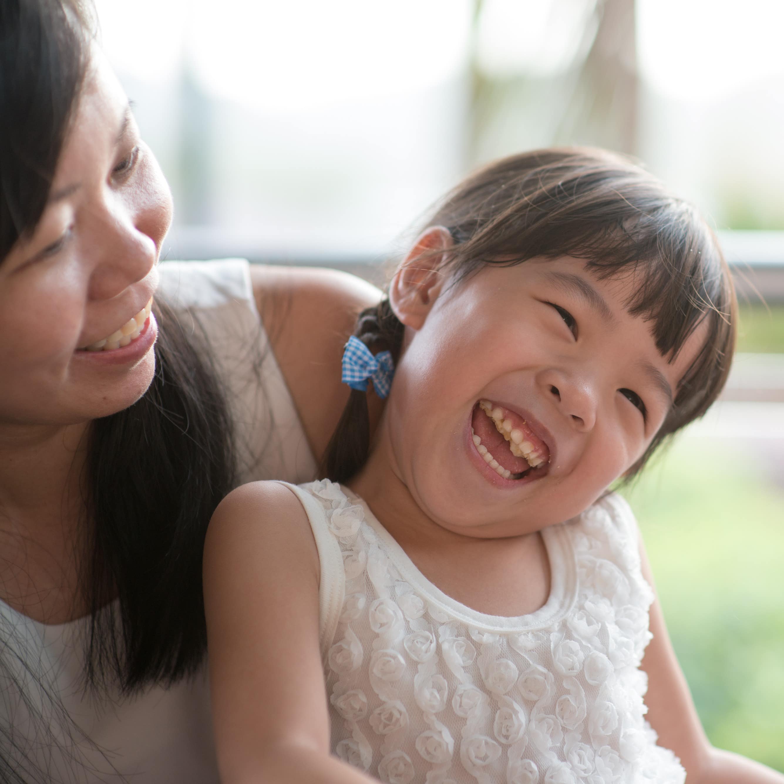 Little girl giggling in mom’s lap while eating at the restaurant outside