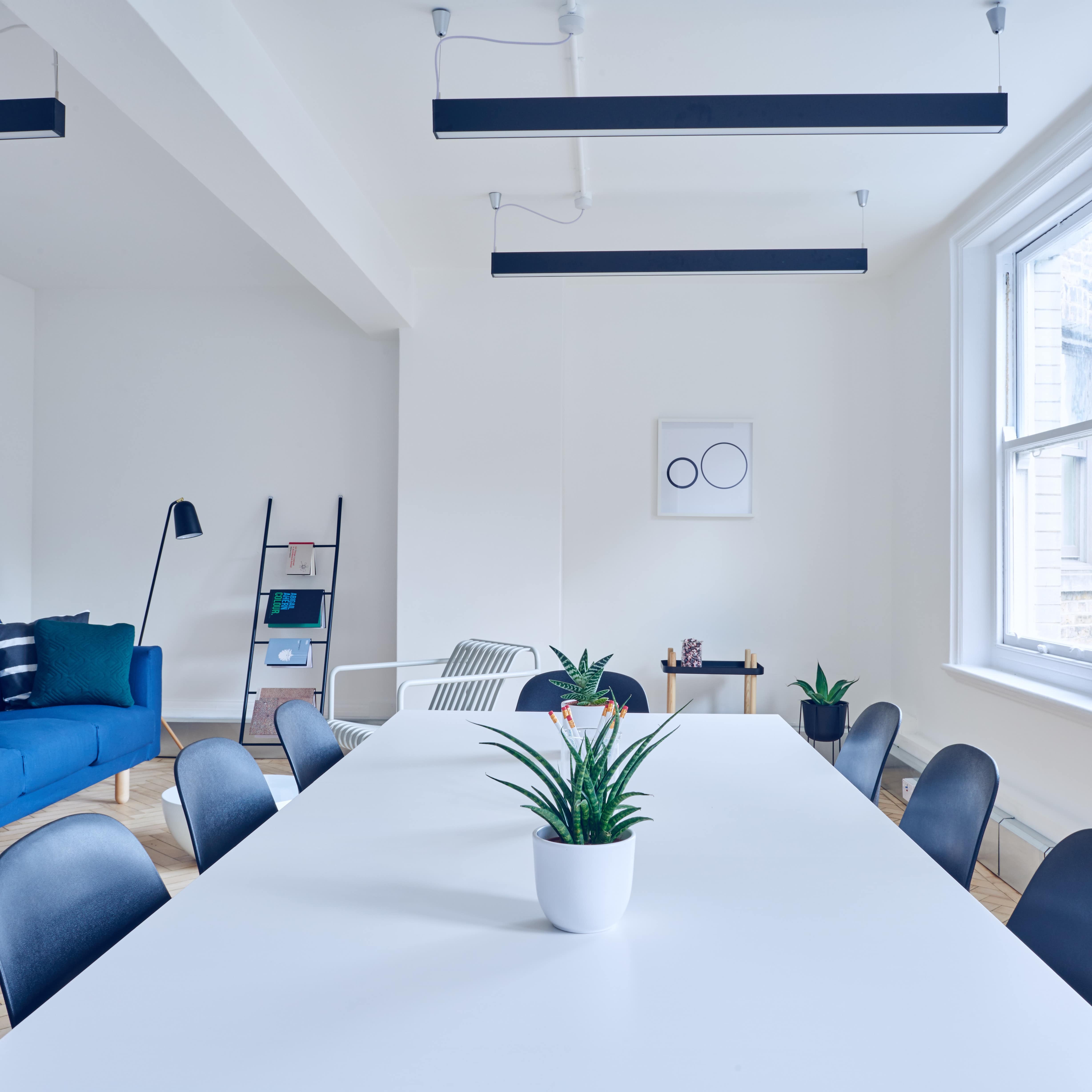 Modern apartment with open living and dining areas, a long white table with blue chairs, a royal blue sofa and a large window