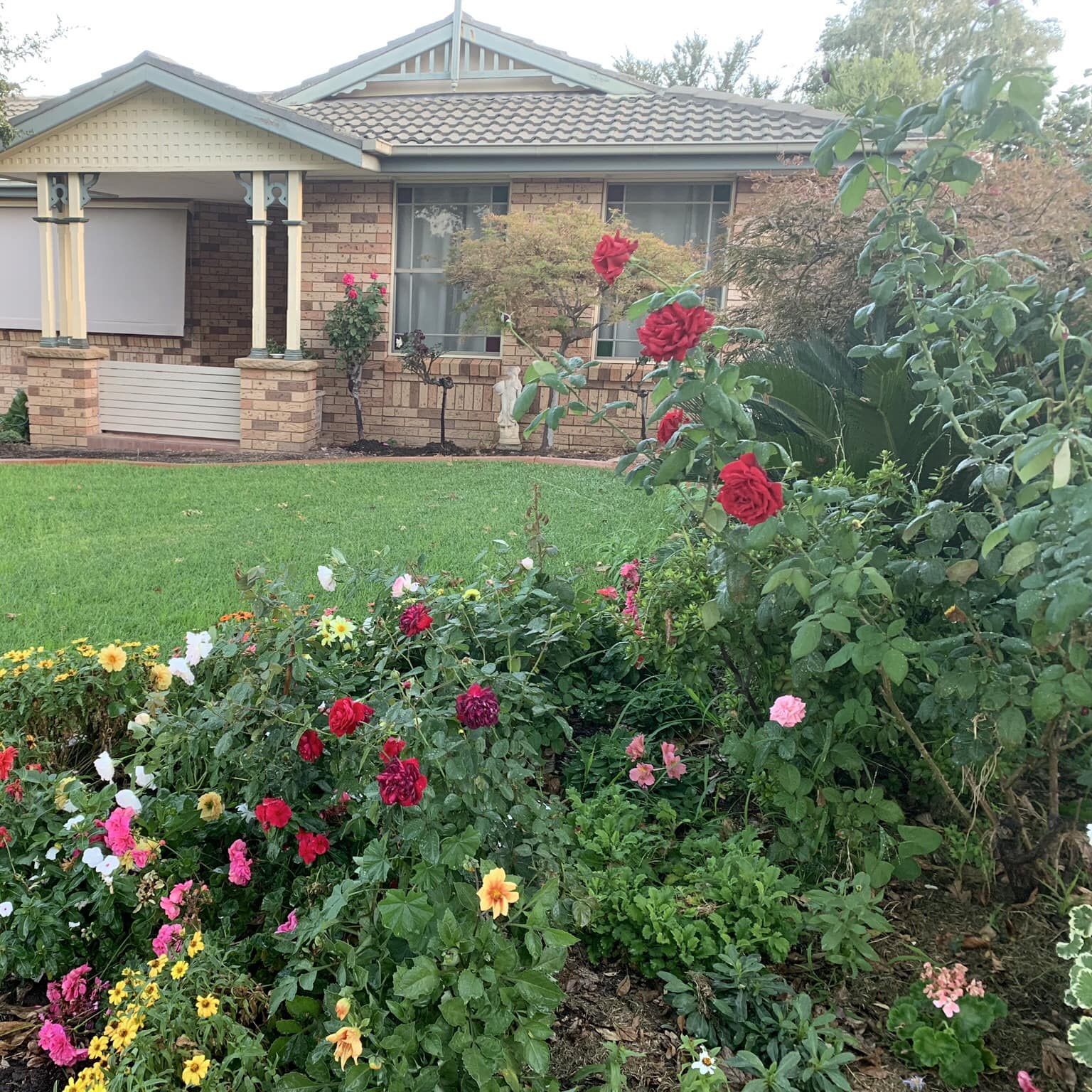 Exterior of ranch-style home with tan brick siding and shingle roof, landscaped lawn and rose garden.