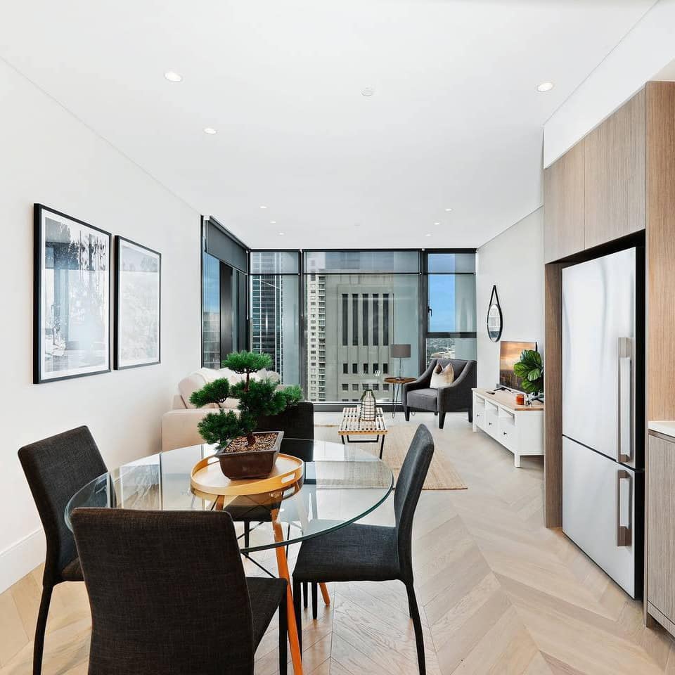 Open kitchen and living room with chevron wood floors, glass dining set, wood cabinets, and tall windows.