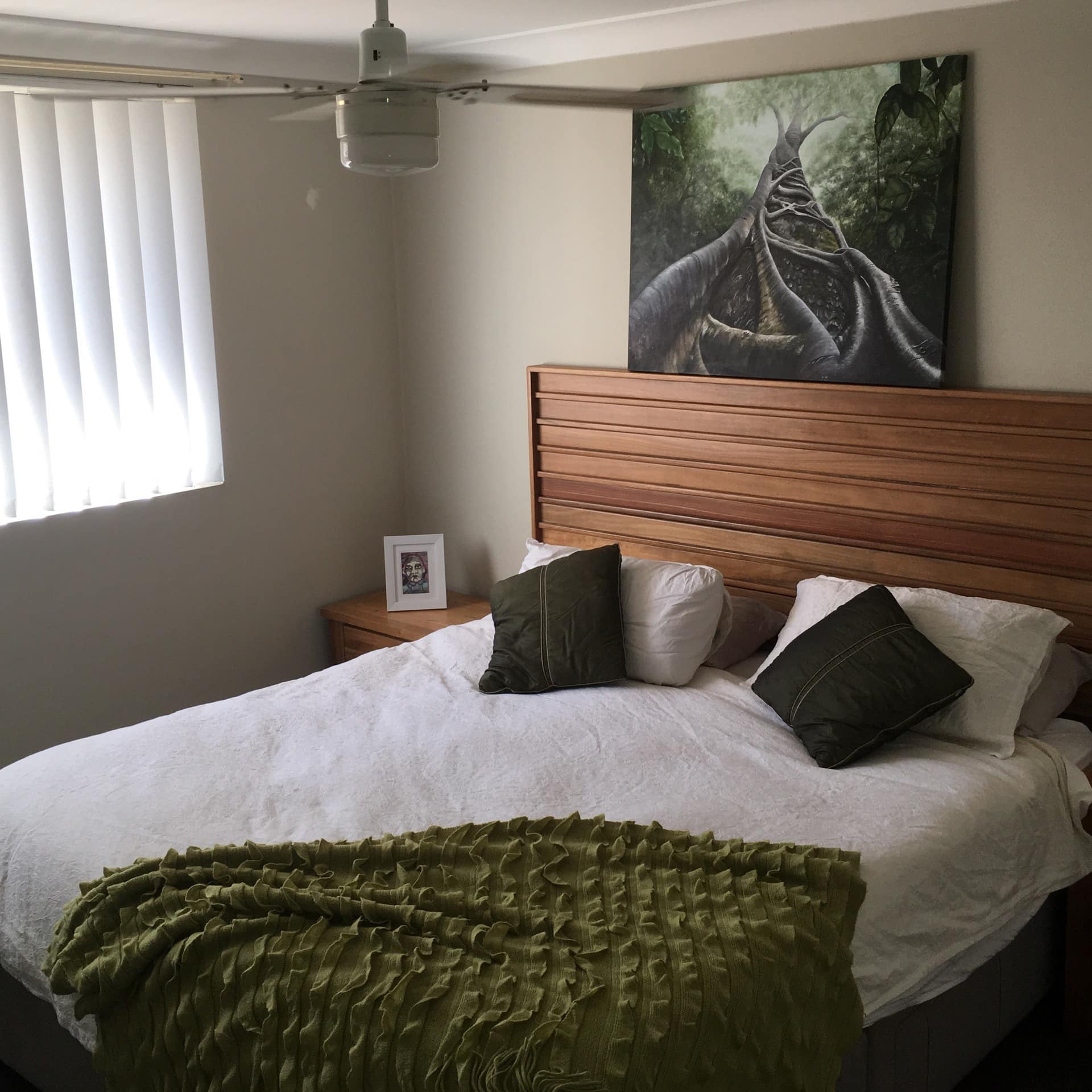 Bedroom with beige walls, a queen-size bed with a wood-panelled headboard, and dark green and white decor.
