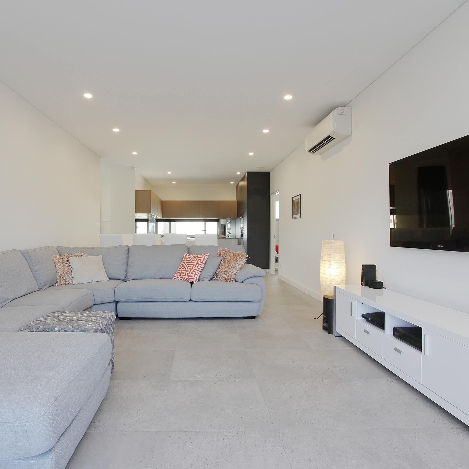 Spacious living room with grey tile floors, a grey sectional, flatscreen TV, and white TV stand.