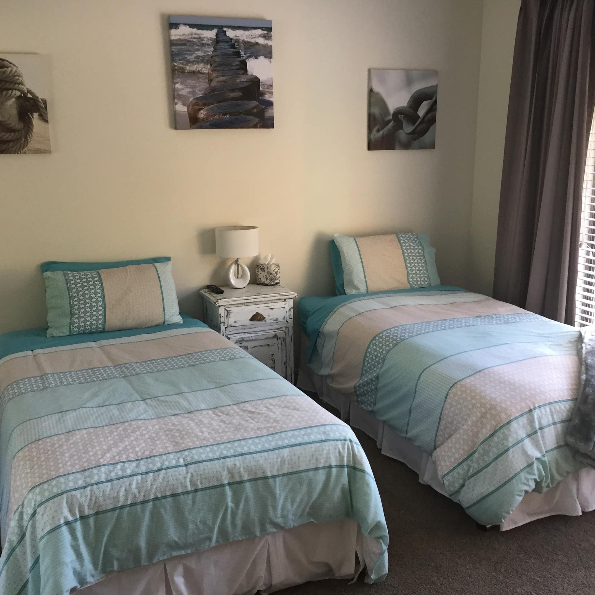 Bedroom with two twin beds, teal comforters, grey carpet, beige walls, and black and white photos above the beds.