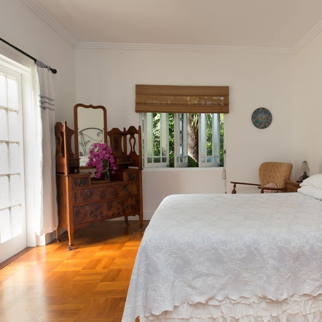 Bedroom with parquet wood floors, white walls vintage furniture, king size bed, french glass doors, small window.
