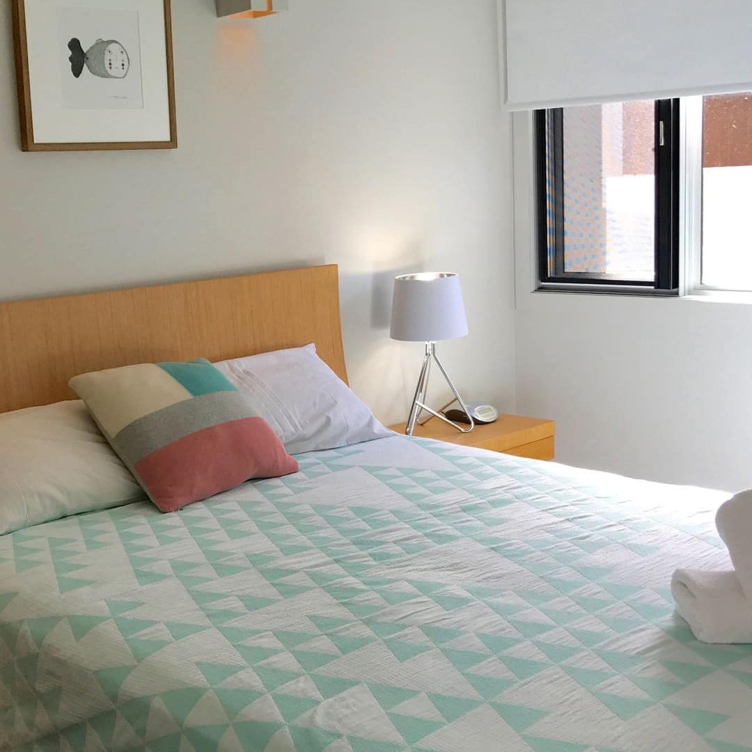 Bedroom with white walls, wood-framed queen size bed, white and teal bedding, matching wood bedside tables.