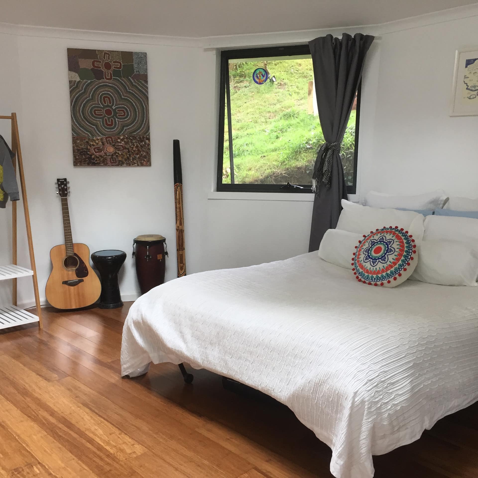 Large, comfortable bed with white linens in 1-bedroom yurt with hardwood floors and window looking out on bushland